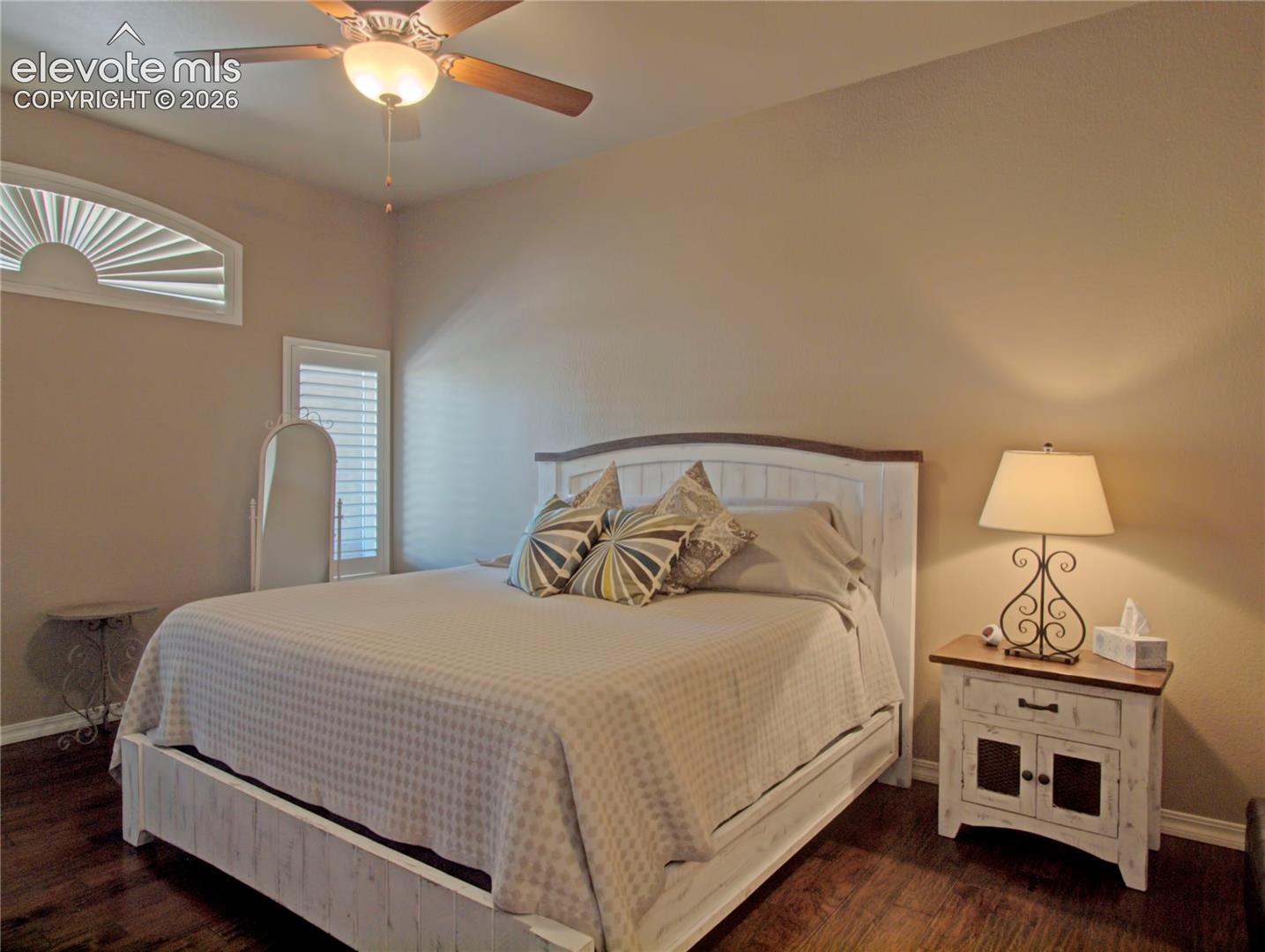 Bedroom featuring wood-finish flooring, a ceiling fan with integrated lighting, and window with plantation shutters. large enough for a king size bed.