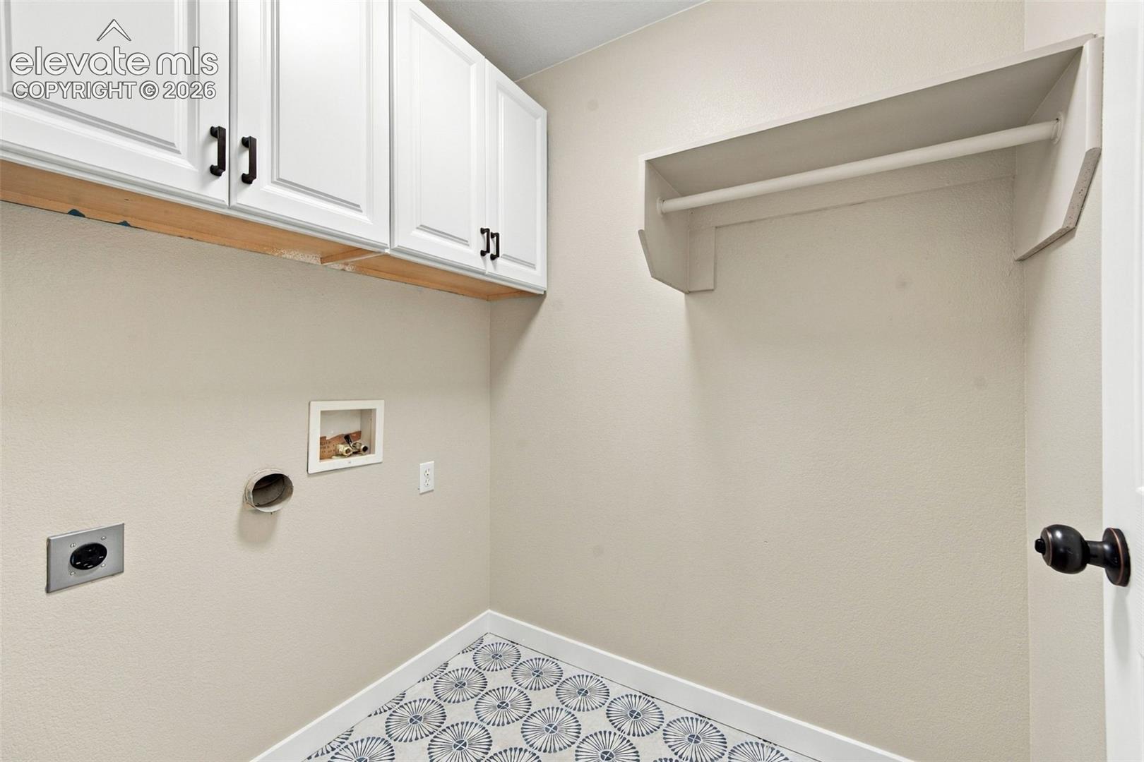 Utility room featuring white shaker-style wall-mounted cabinetry with matte black hardware, patterned tile flooring, and a built-in shelf with a hanging rod