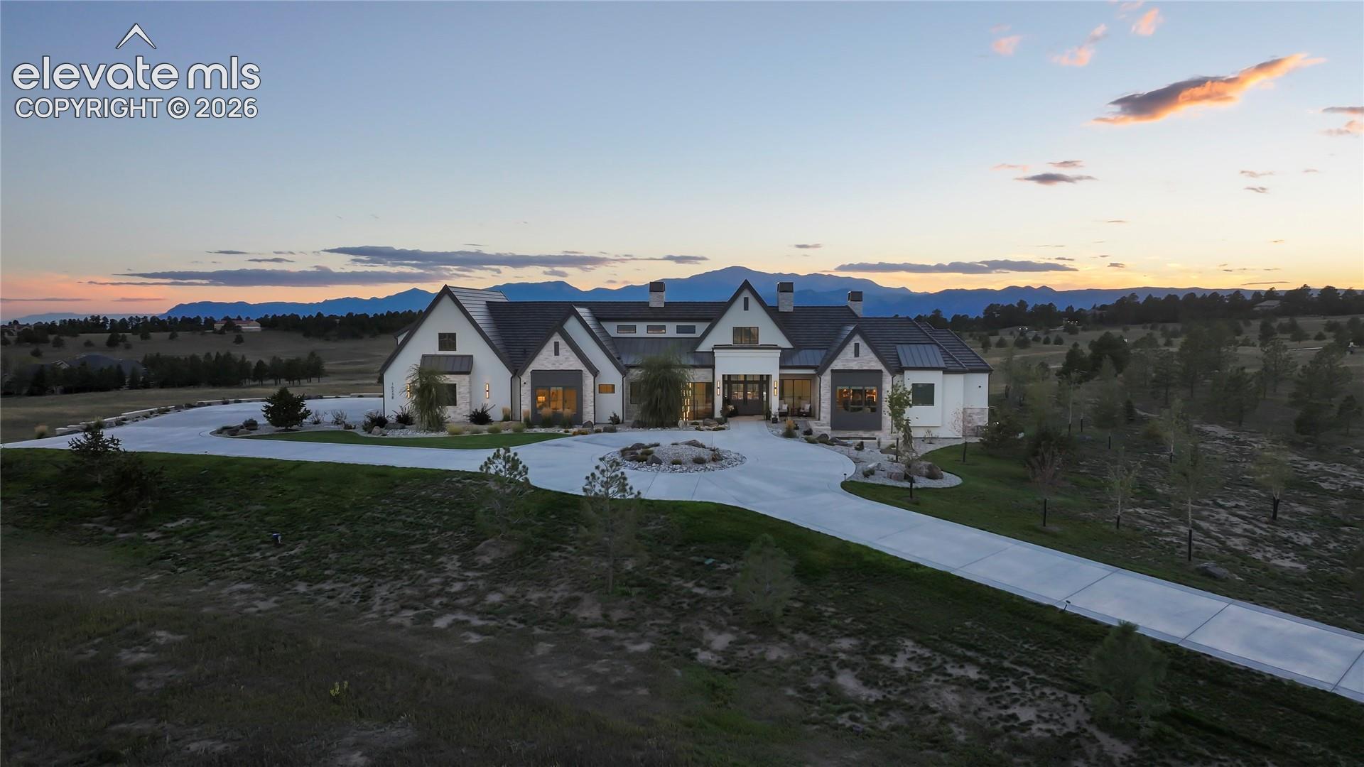 Multi-gabled estate exterior featuring a stucco and stone facade, expansive circular concrete driveway, and prominent mountain backdrop