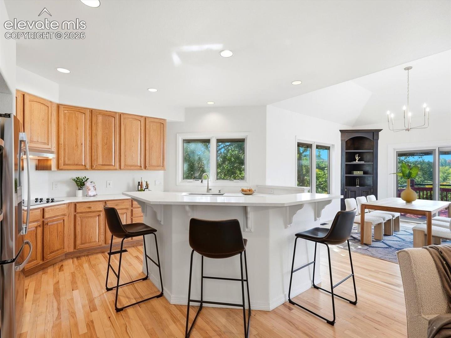 Kitchen featuring light-tone wood cabinetry, solid-surface peninsula with integrated sink, wood-finish flooring, recessed lighting, and a built-in corner display shelving unit