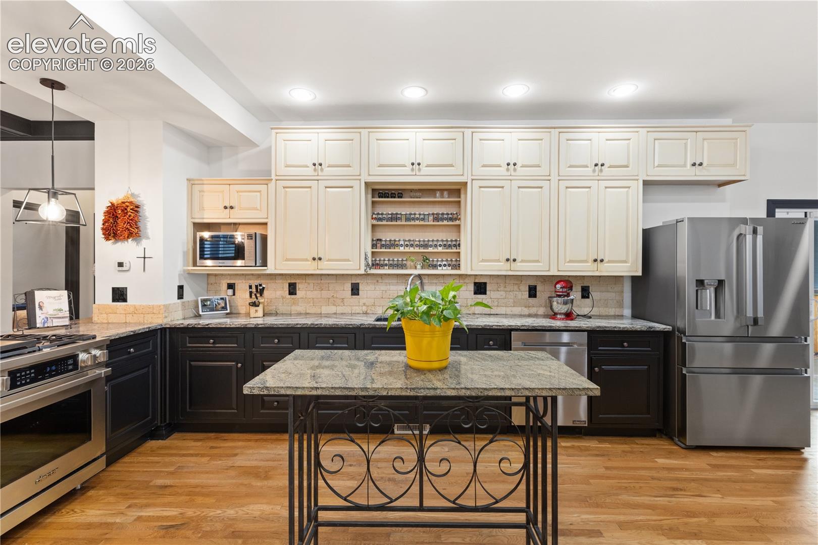 Spacious kitchen featuring wood-finish flooring, two-tone cabinetry, stone countertops, a subway tile backsplash, and stainless steel appliances