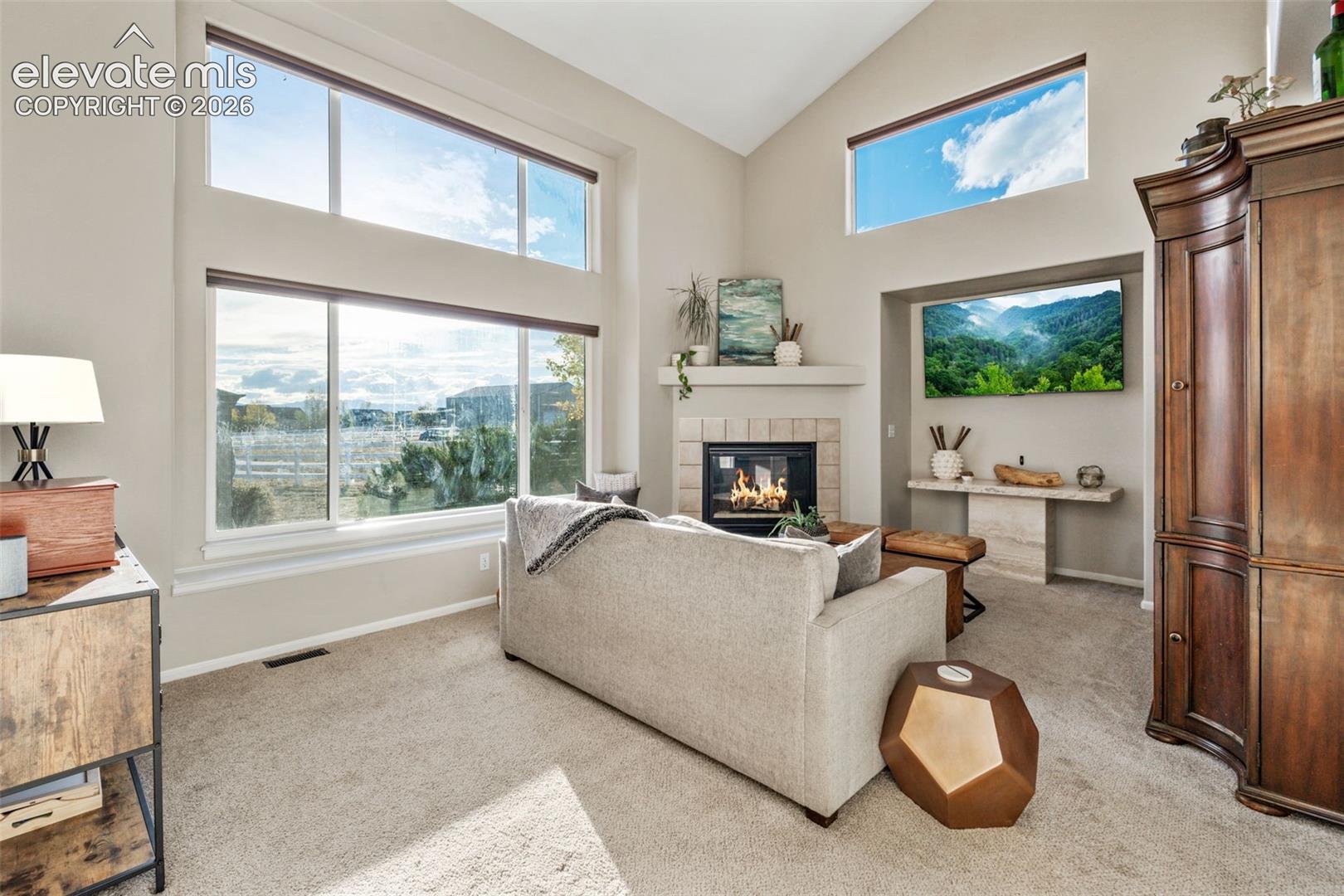 Vaulted ceilings featuring expansive stacked windows, stone-surround fireplace with a mantel, and built-in stone console shelf