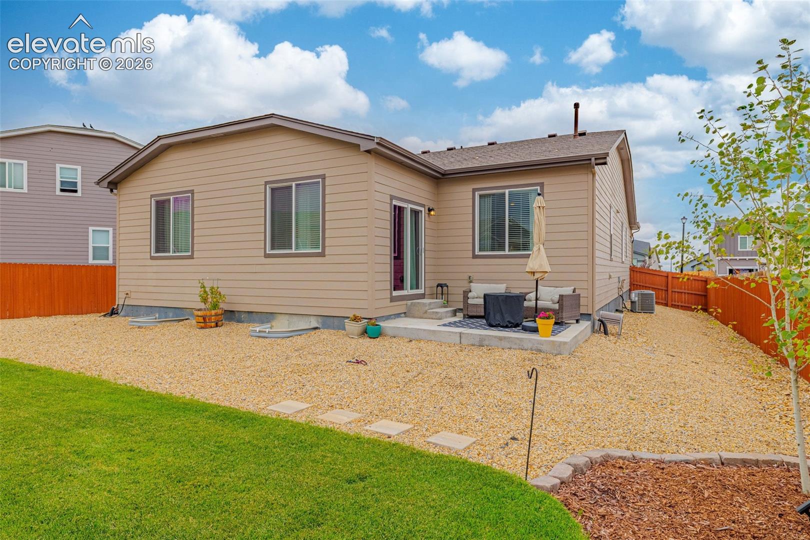 Tan siding exterior with a concrete patio, sliding glass door, and a brown privacy fence
