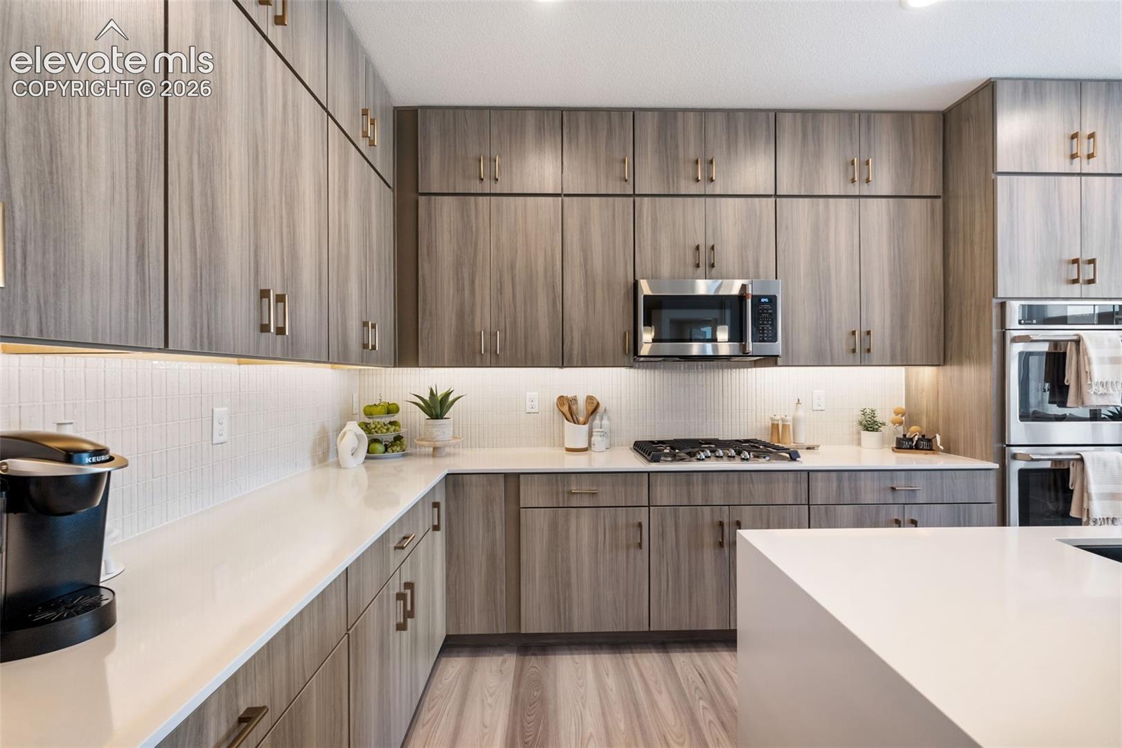 Kitchen featuring wood-finish cabinetry, white solid-surface countertops, vertical-tile backsplash, built-in stainless steel double oven, and integrated gas cooktop