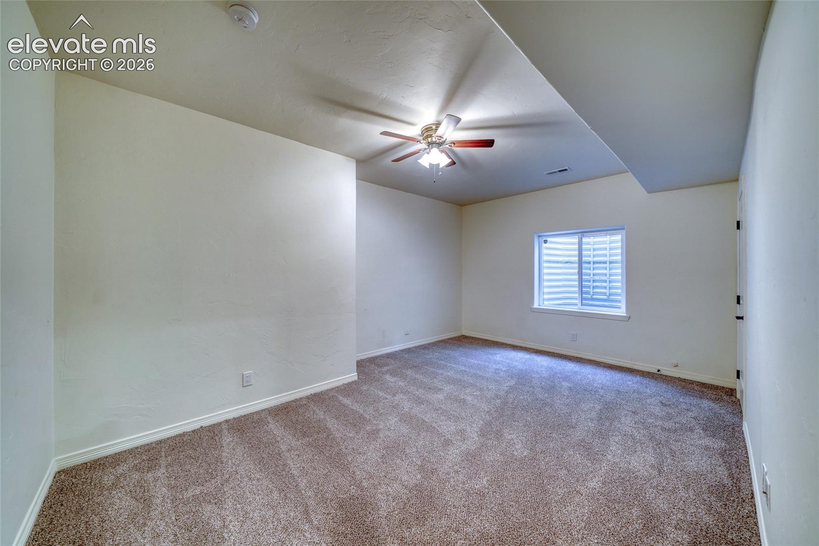 Wall-to-wall carpeting, window with blinds, ceiling fan with integrated lighting, and neutral wall tones