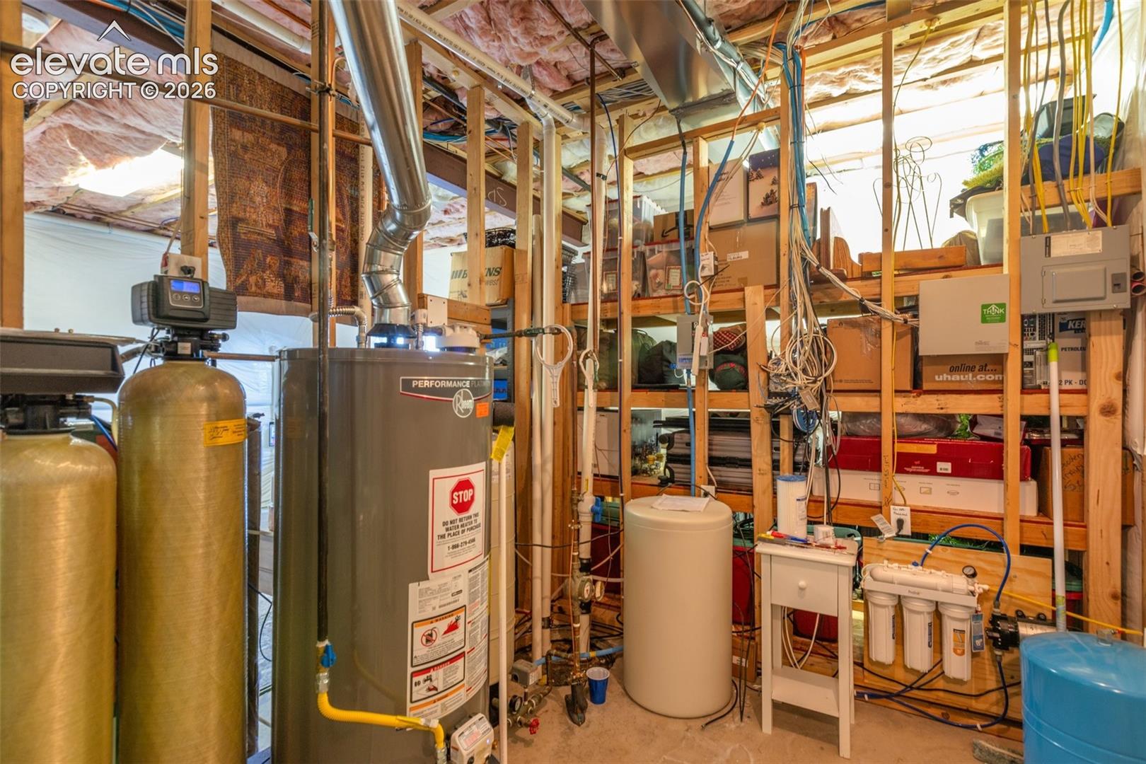 Utility area featuring a water heater, water softener system, filtration unit, and exposed wood-frame wall construction