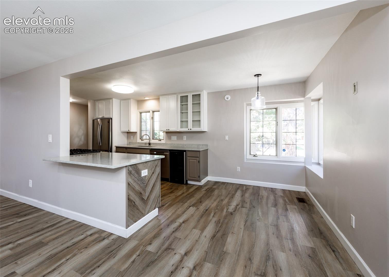 Wood-finish flooring throughout, kitchen with light-tone upper cabinetry, lower cabinetry, and stainless steel appliances