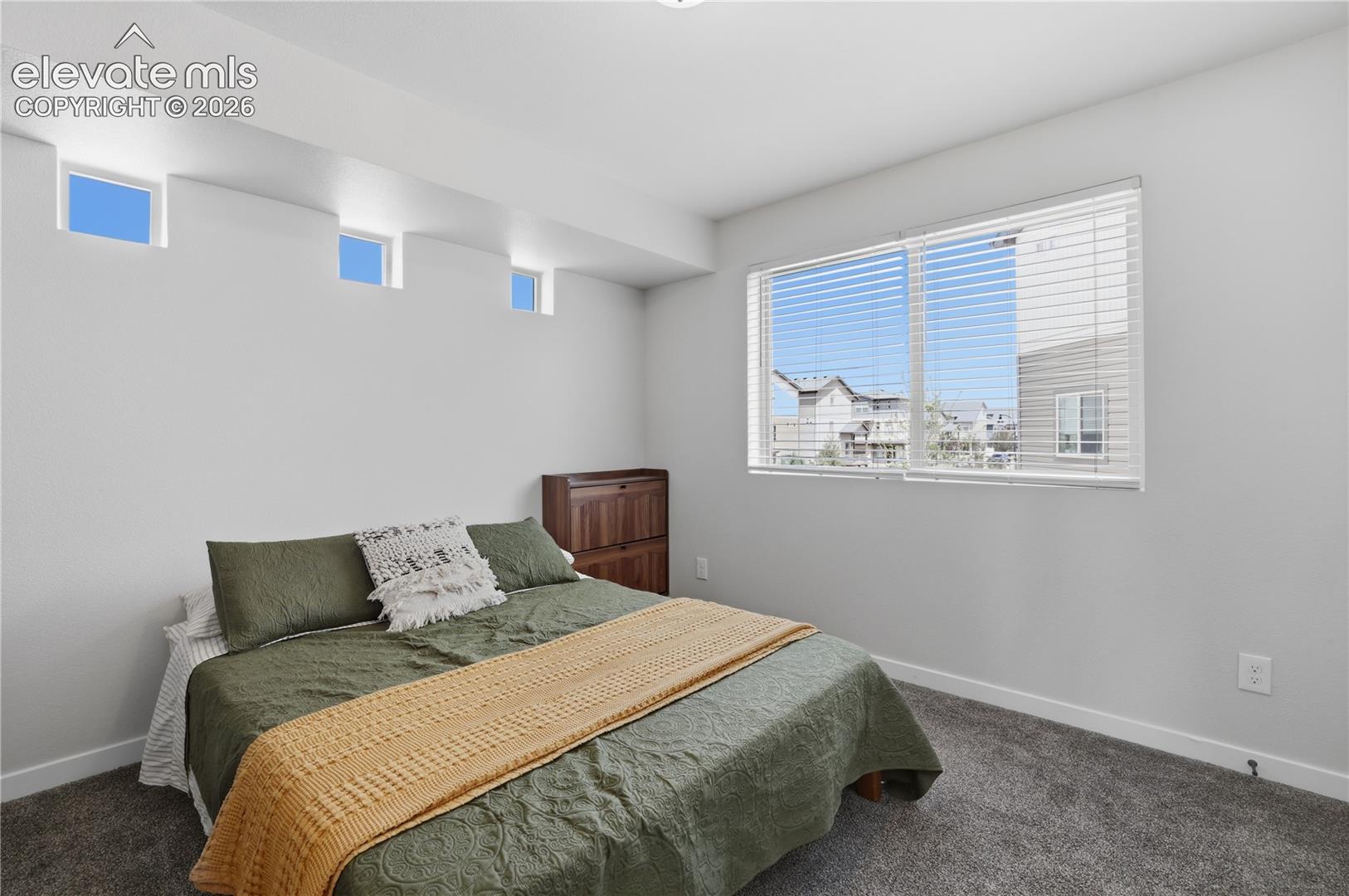 Spacious room featuring a large window with blinds, three transom windows, light gray walls, dark gray carpet, and white baseboards