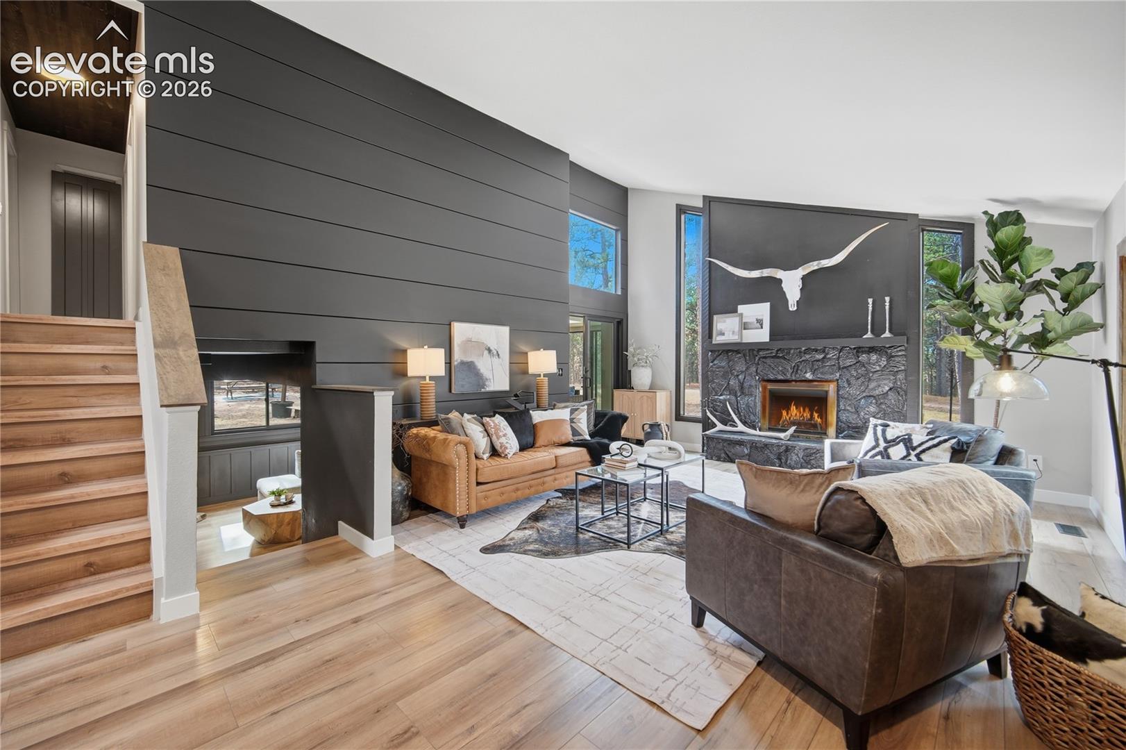 Vaulted ceilings, wood-finish flooring, floor-to-ceiling dark horizontal paneling, and a stone-clad fireplace