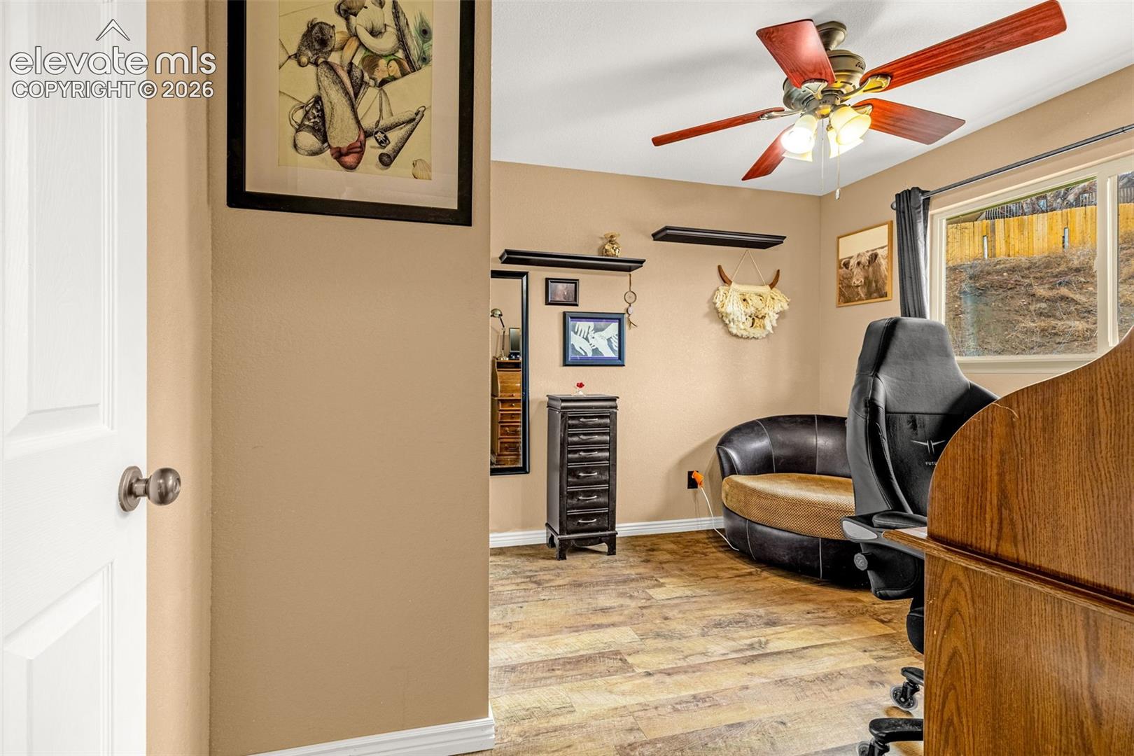 Room featuring wood-finish flooring, a ceiling fan with integrated light fixture, dual wall-mounted floating shelves, and a multi-pane window