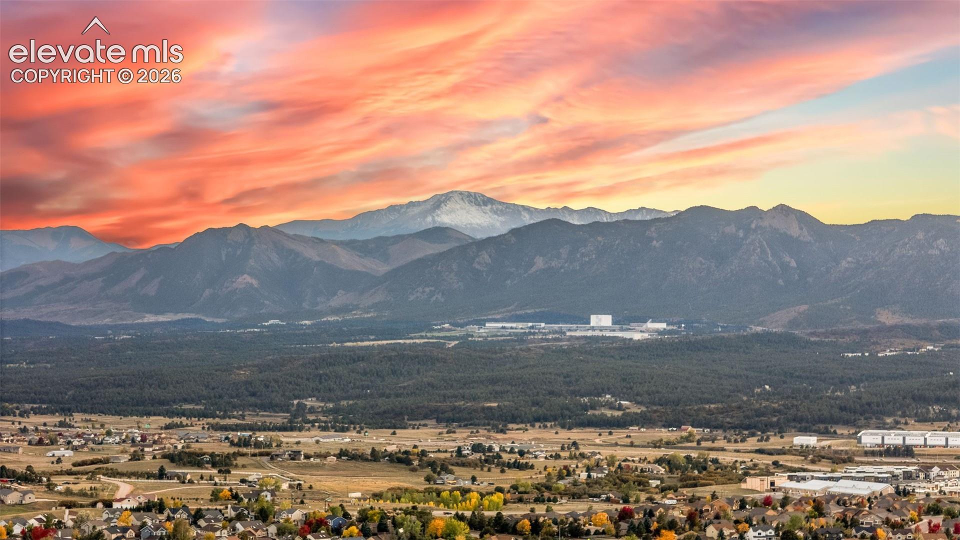Panoramic mountain backdrop featuring prominent peaks and expansive treed terrain under a colorful sky