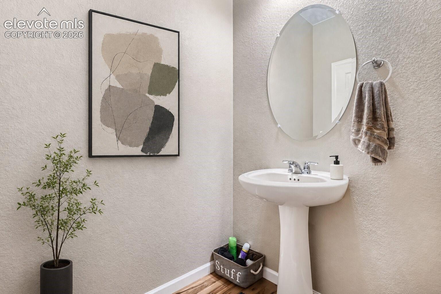 Pedestal sink with a polished chrome faucet, wall-mounted oval mirror, and wood-finish flooring