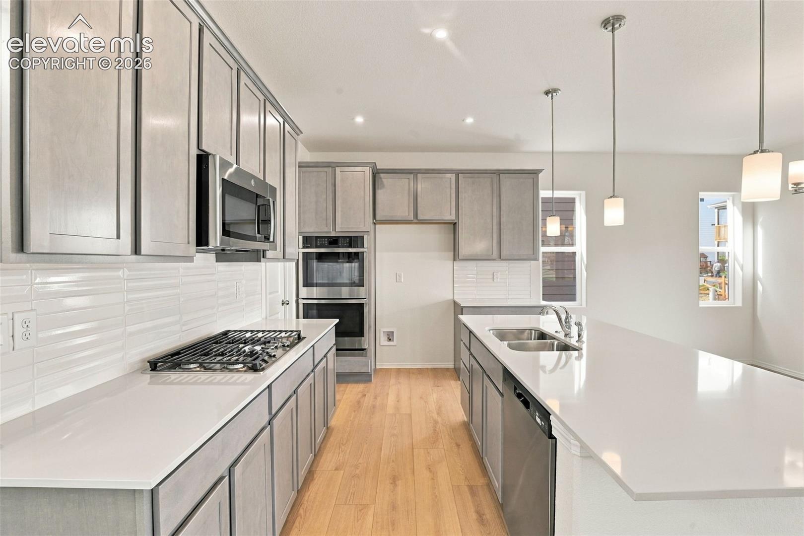 Kitchen featuring shaker-style cabinetry, quartz countertops, subway tile backsplash, stainless steel appliances including a double wall oven and gas cooktop, and an oversized island with pendant lighting
