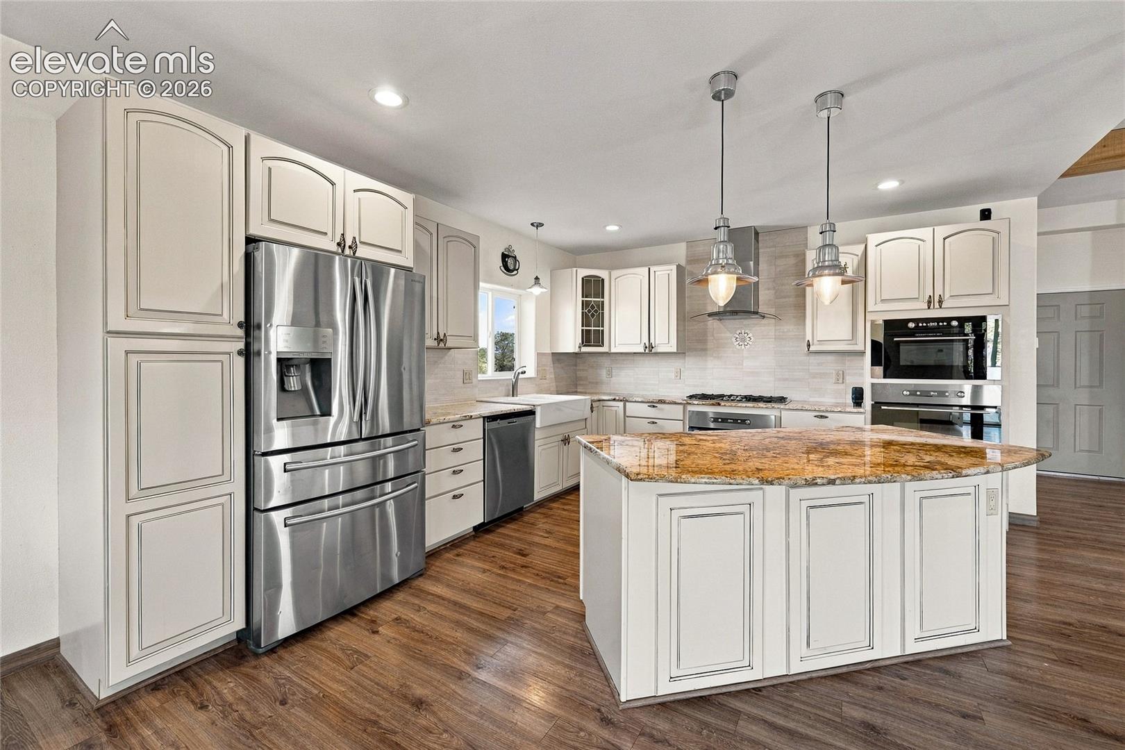 Kitchen featuring cream-toned cabinetry, a center island with a stone countertop, wood-finish flooring, stainless steel appliances, and dual pendant lighting