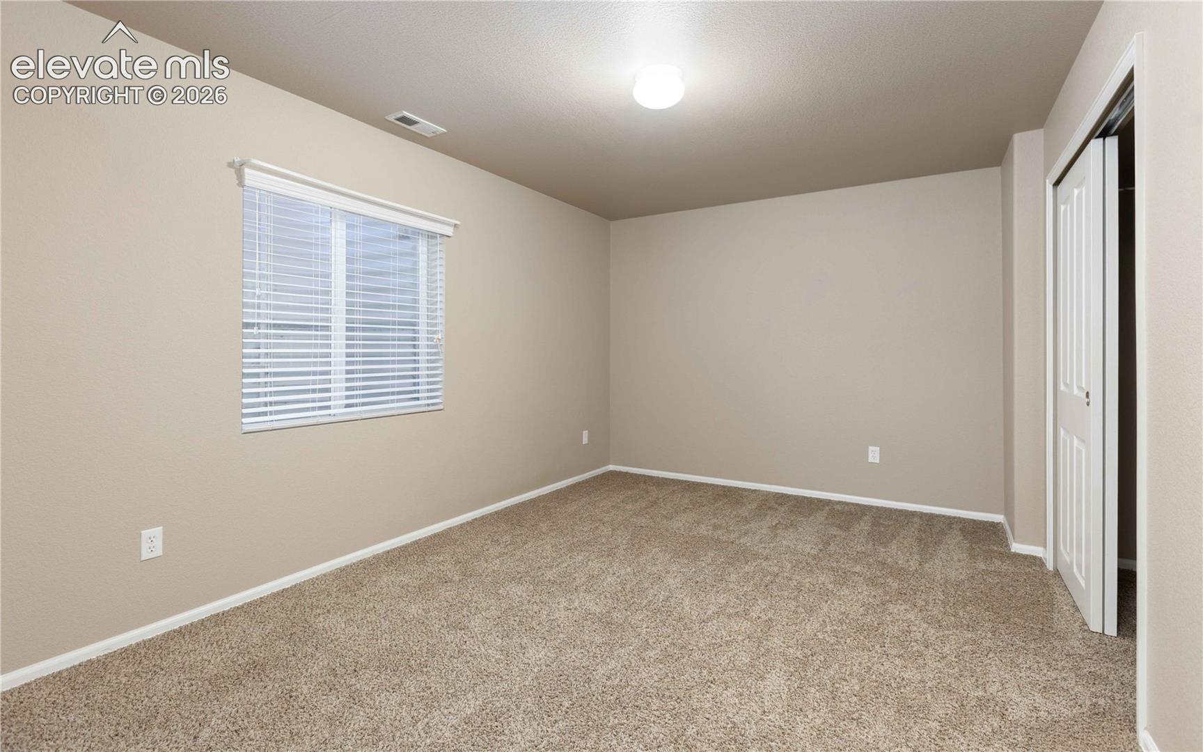 Neutral-toned interior space featuring neutral wall-to-wall carpeting, a single-window with horizontal blinds, and a closet with a bifold door