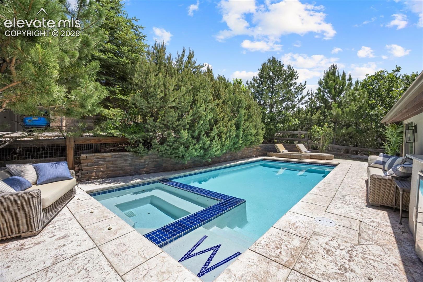 Outdoor swimming pool featuring a built-in spa with blue mosaic tiling and a stamped concrete patio surround