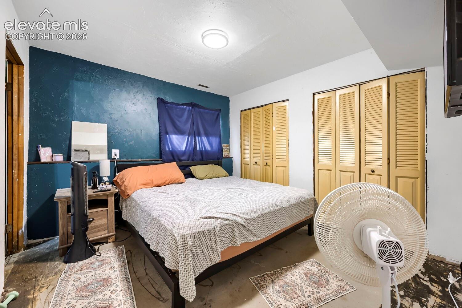 Bedroom featuring a textured accent wall, two sets of louvered bi-fold closet doors, and recessed ceiling lighting