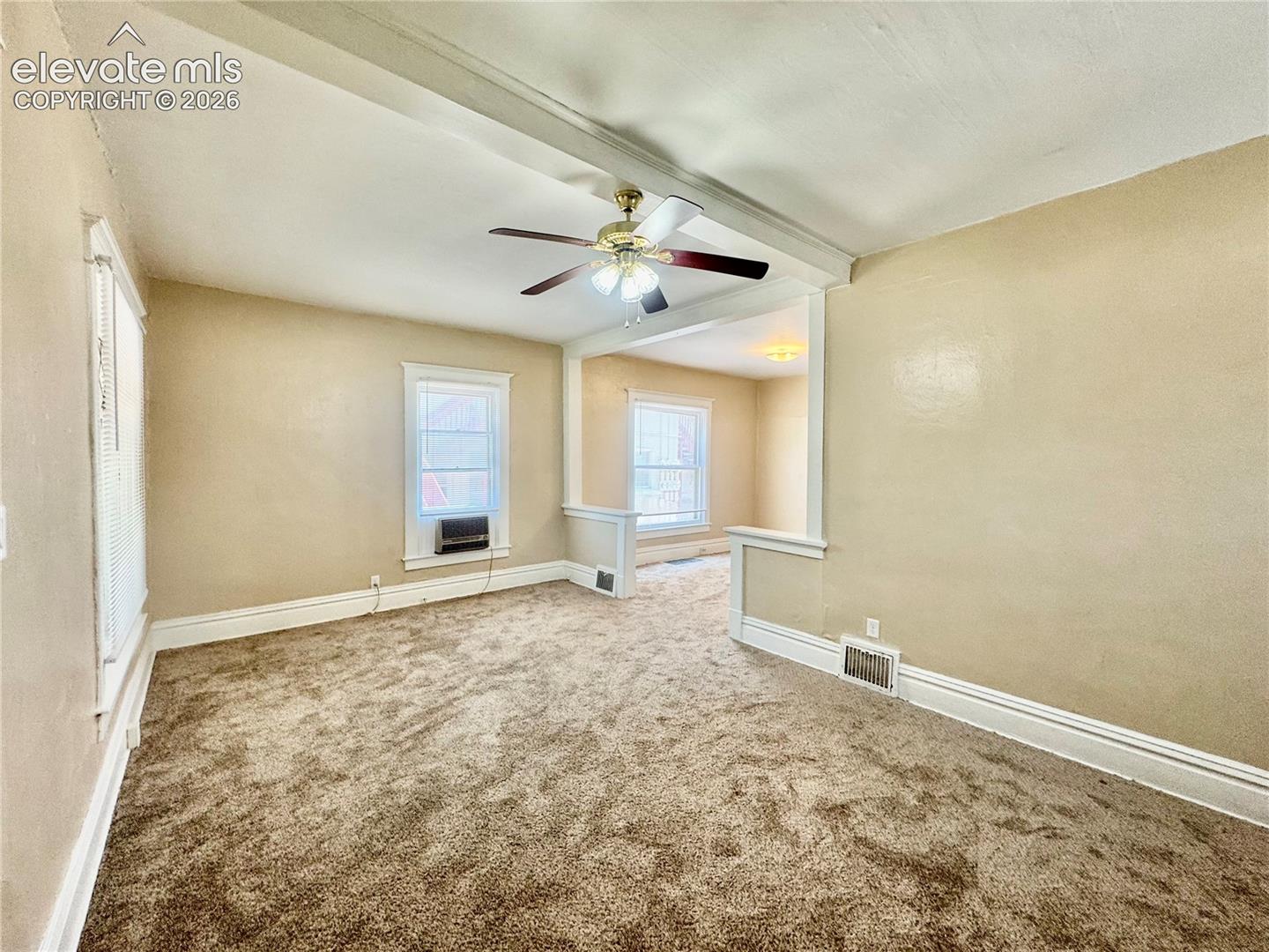 Spacious room featuring neutral wall finishes, plush carpet flooring, ceiling fan with integrated lighting, and multiple windows providing natural illumination