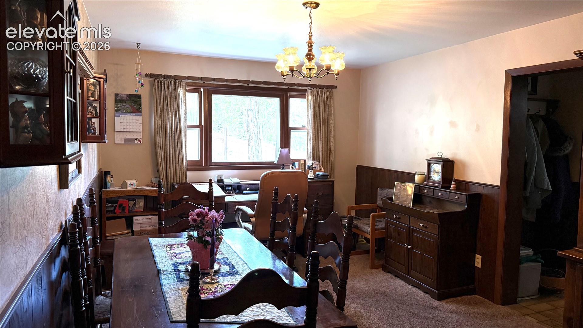 Dining area featuring wood-finish paneling, a multi-pane window, and a chandelier light fixture