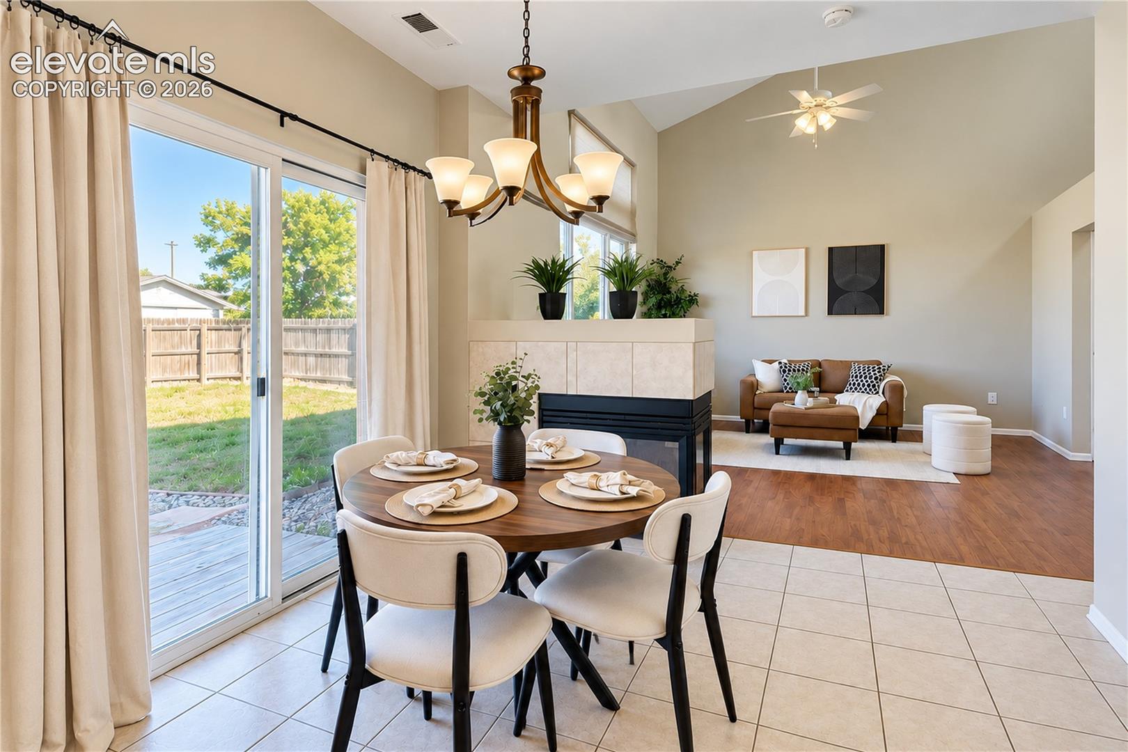 Vaulted ceilings, tiled dual-sided fireplace, sliding glass door to exterior, wood-finish flooring, and multi-light chandelier