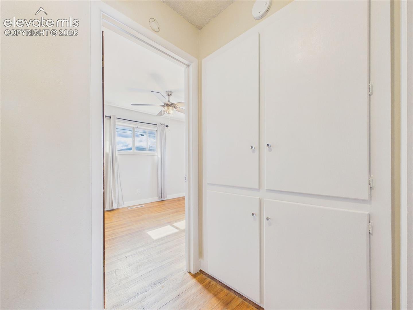 Hallway featuring hardwood flooring, built-in linen cabinets, and convenient access to the adjoining bedroom.