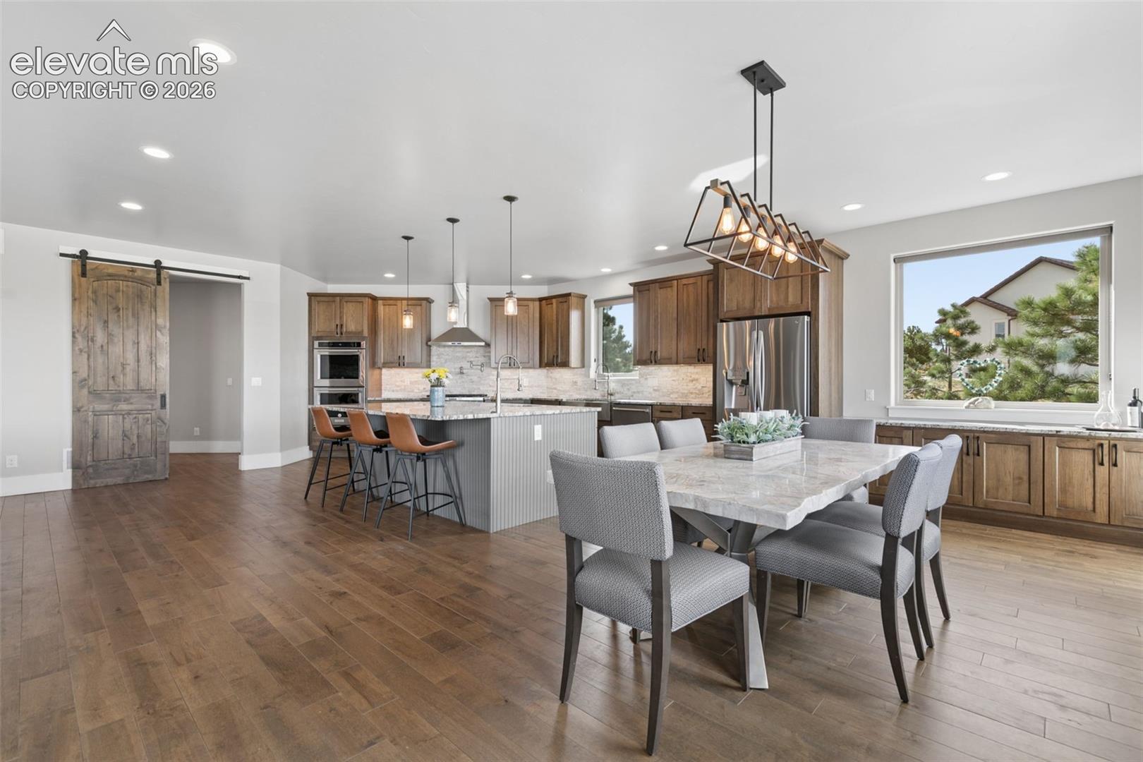 Wood-finish flooring throughout, kitchen island with seating, built-in stainless steel appliances, wood cabinetry, and a sliding barn door