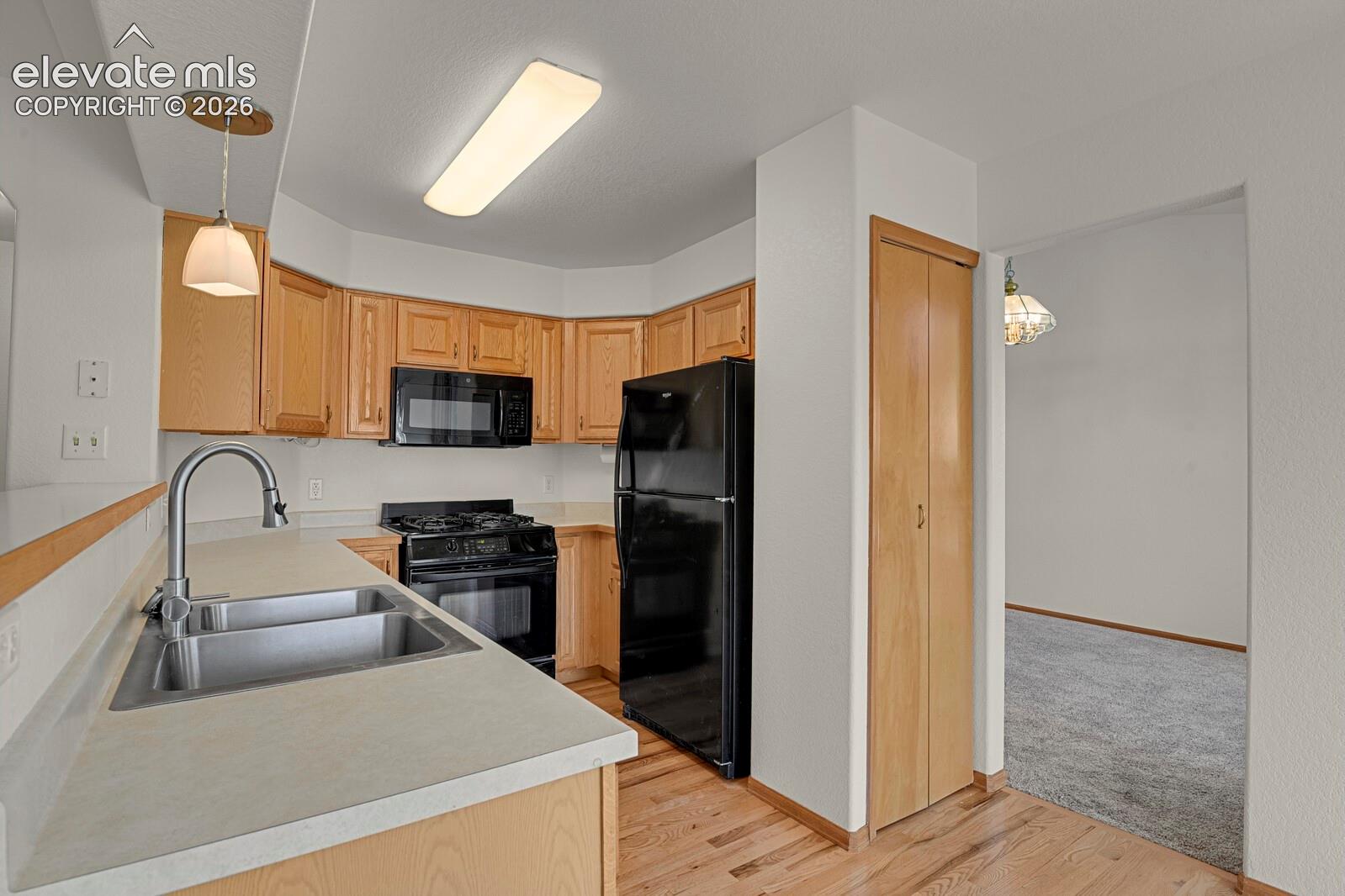 Kitchen featuring wood cabinetry, stainless steel double basin sink, black appliances, and wood-finish flooring