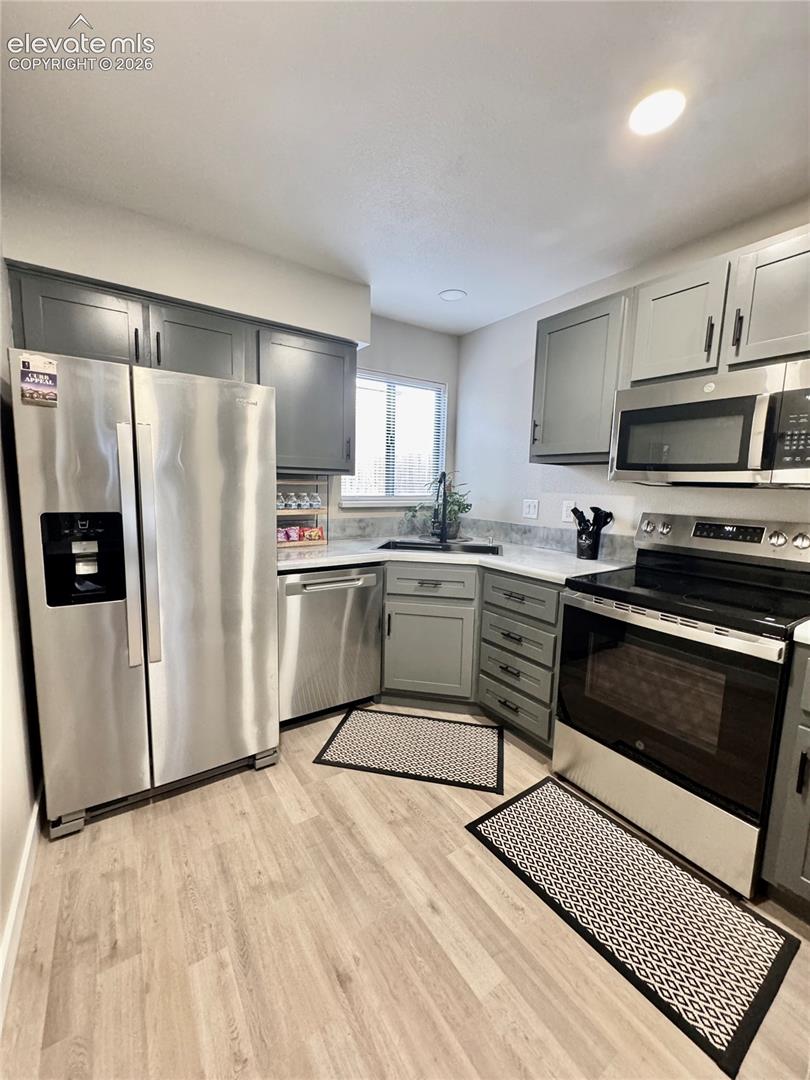 Kitchen featuring grey cabinetry, stainless steel appliances, light-toned stone-finish countertops, and wood-finish flooring