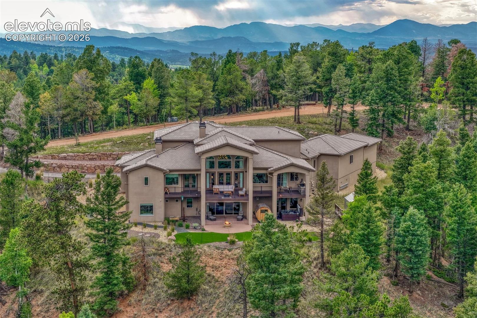 Expansive multi-level structure with a stucco exterior, multiple balconies, a lower-level patio, and surrounding mature trees