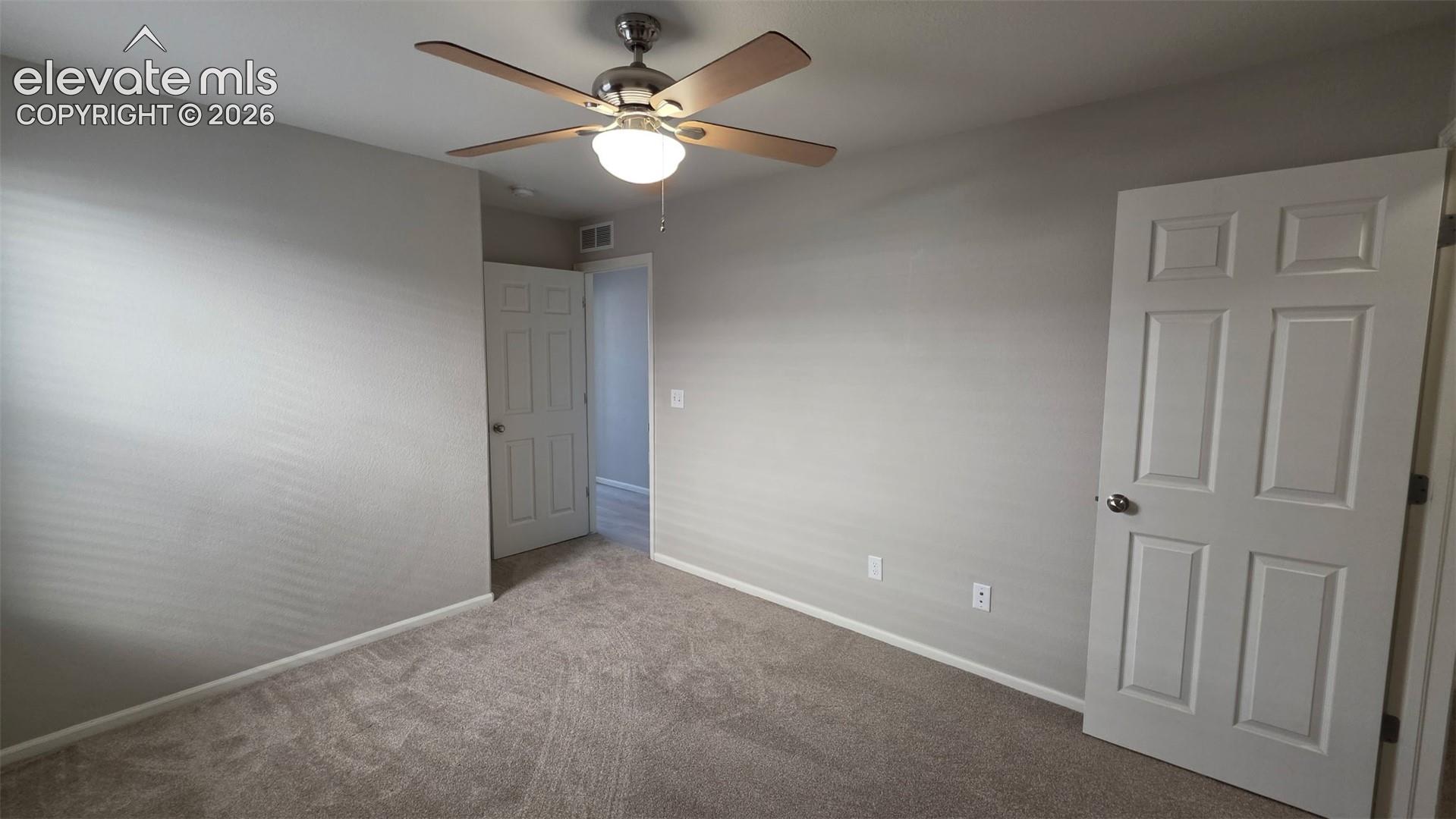 Room featuring neutral-toned carpeting, two six-panel interior doors, and a ceiling-mounted fan with integrated lighting