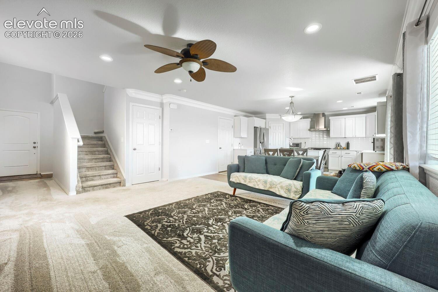 Open-concept interior featuring recessed lighting, a multi-blade ceiling fan, crown molding, and white kitchen cabinetry
