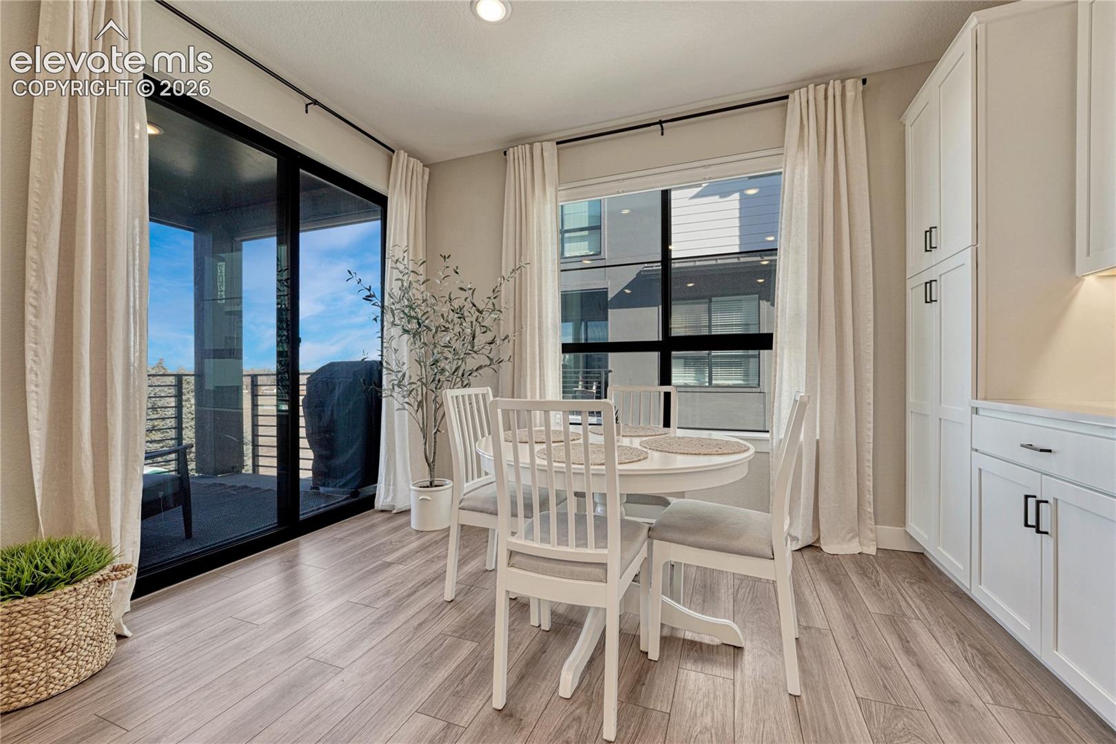 Wood-finish flooring, full-height white cabinetry with integrated hardware, expansive floor-to-ceiling windows, and sliding glass door with external balcony access