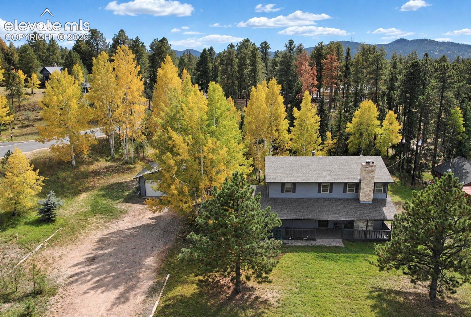 Expansive exterior with a gray-sided residence, stone chimney, and a dark-colored deck