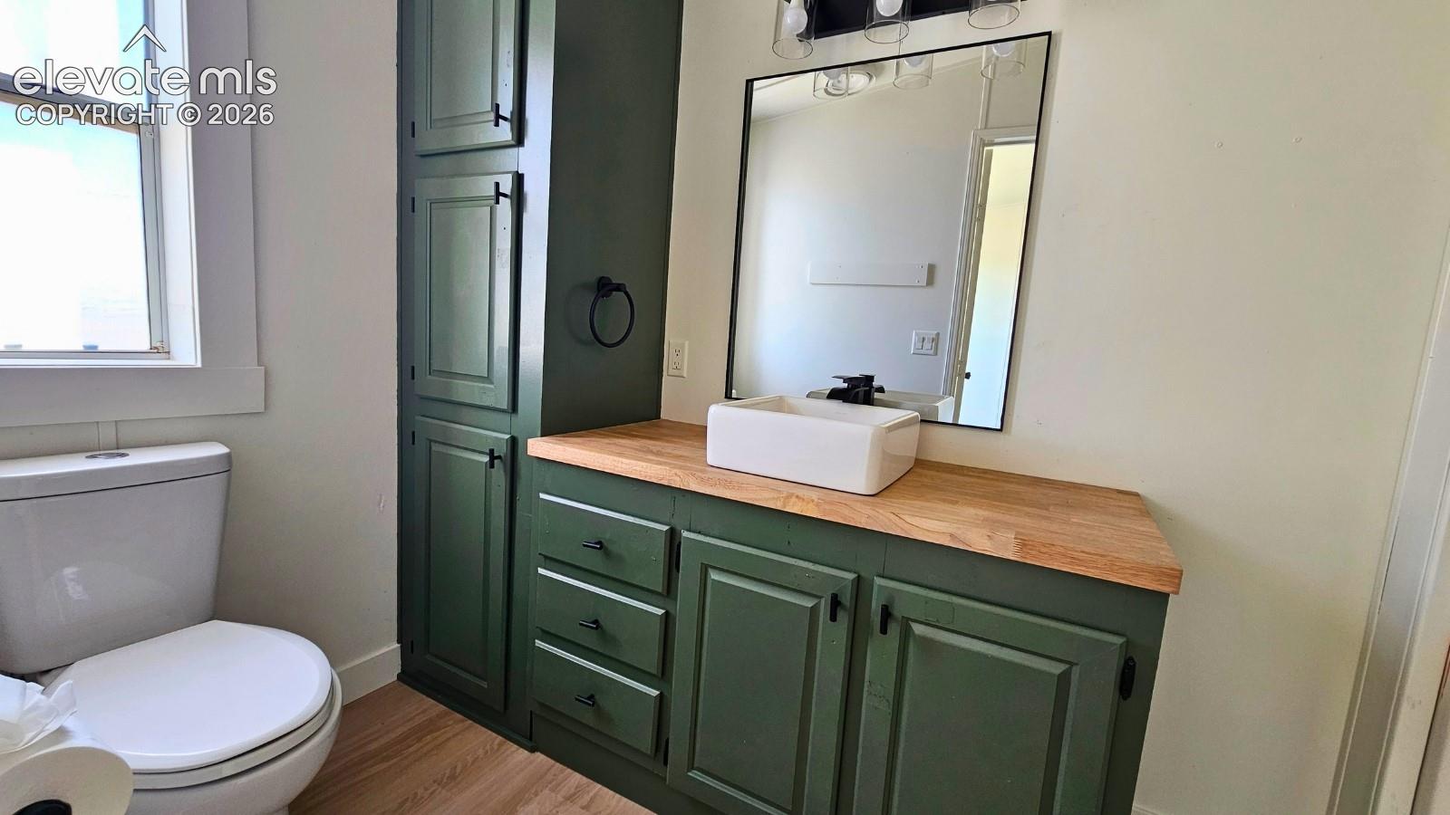 Spa-inspired bathroom featuring custom cabinetry with deep green painted finishes, wood-top countertop, vessel sink, and large framed mirror
