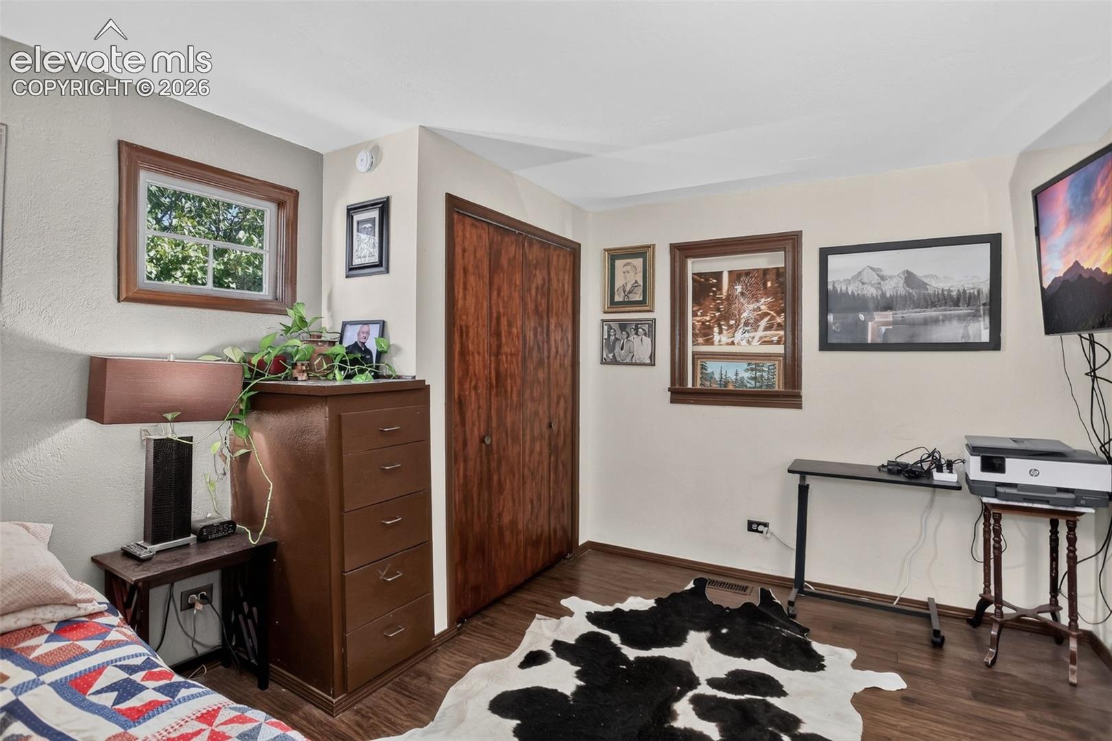 Wood-finish flooring with a smooth texture, two windows with wood trim, a built-in closet with wood-finish doors, and neutral-toned wall paint