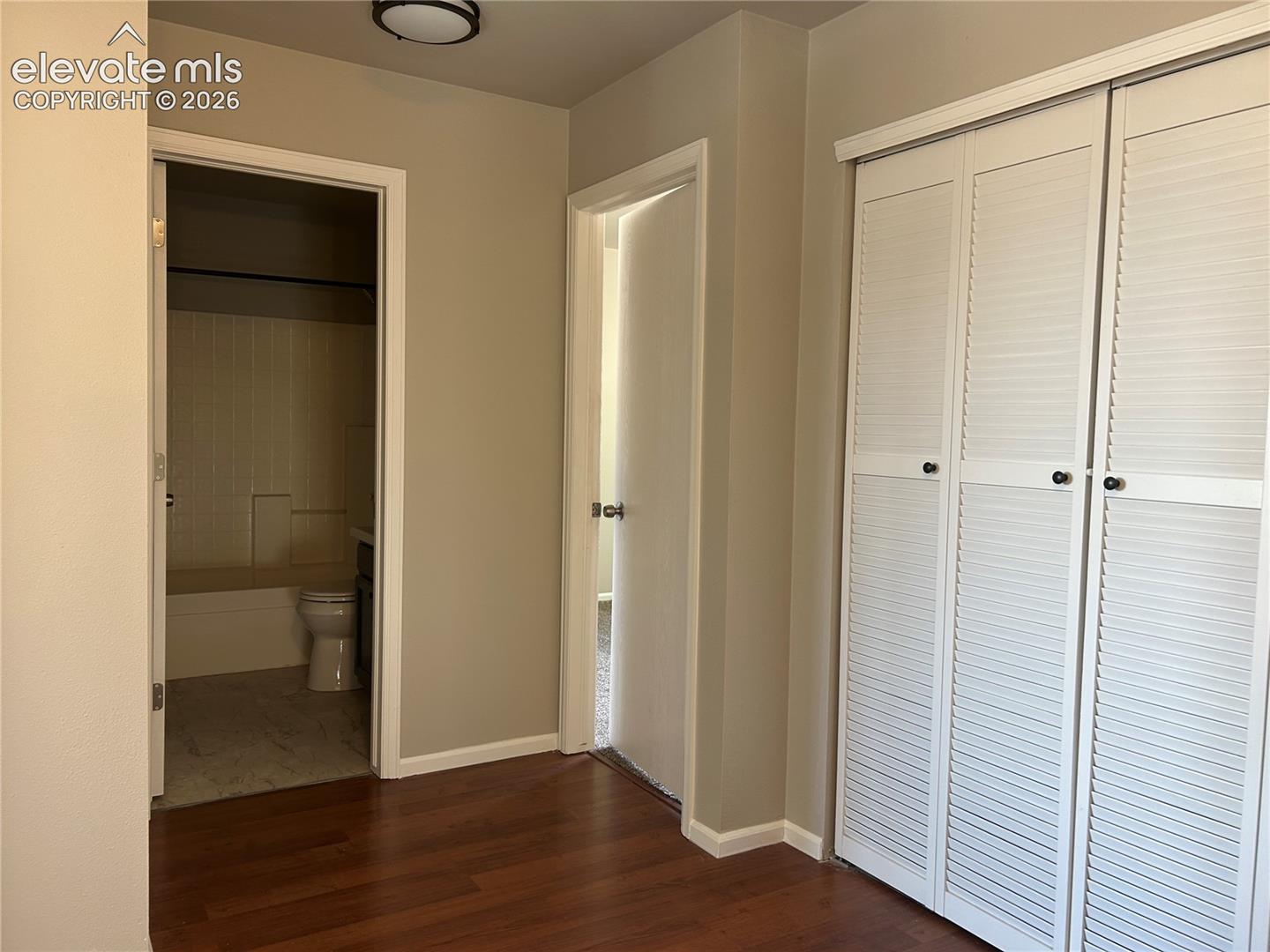Interior space featuring wood-finish flooring, white louvered bifold closet doors, and a bathroom equipped with a shower and tub combination