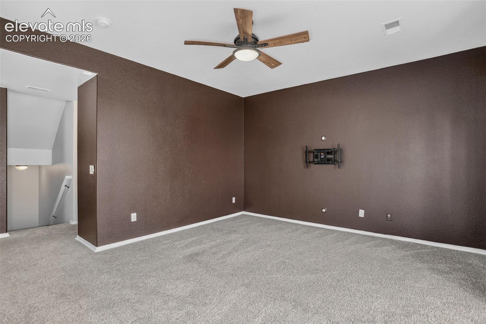 Spacious bedroom with rich chocolate-toned walls, neutral carpeting, ceiling fan with integrated lighting, and multiple electrical outlets