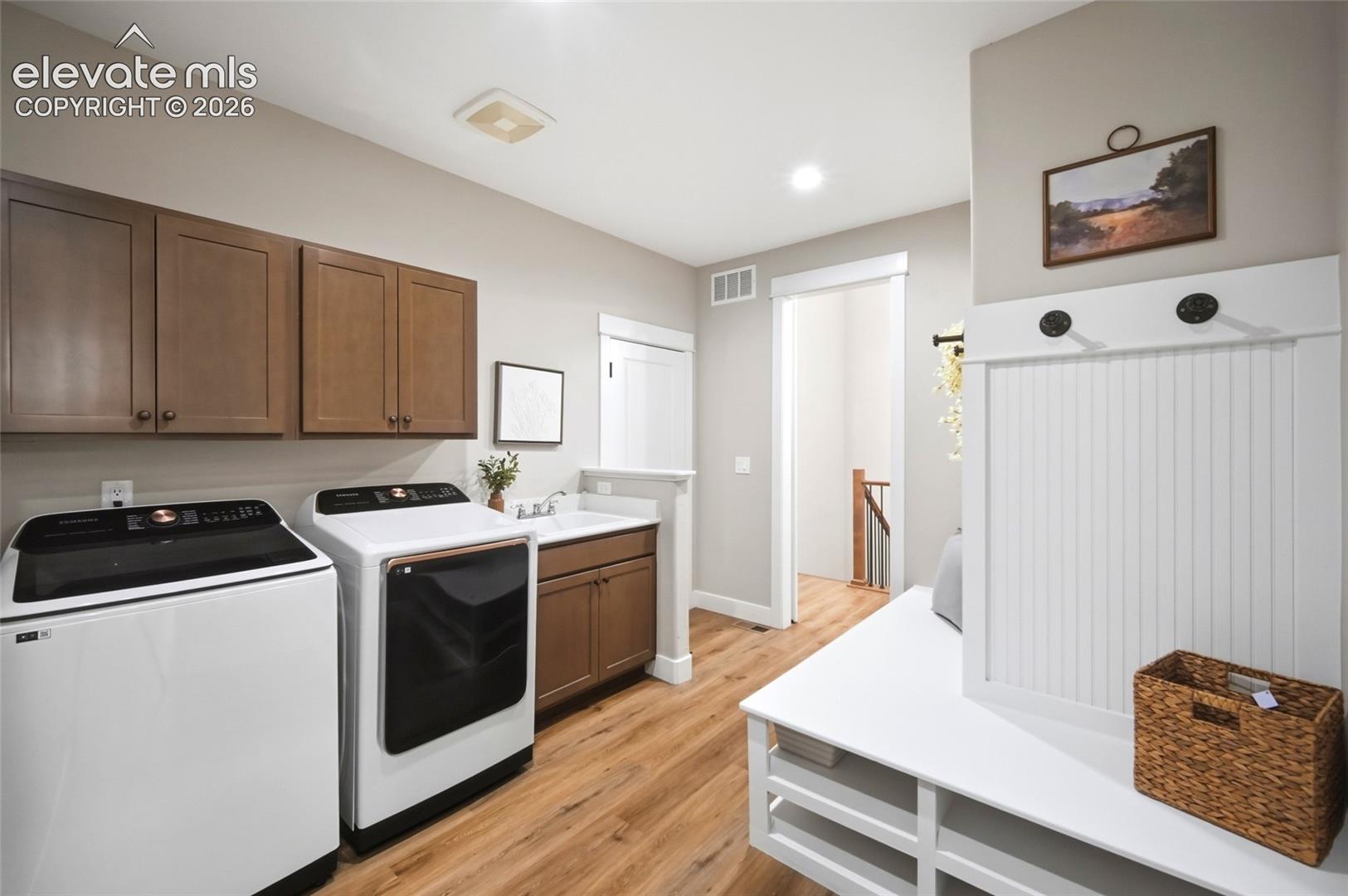Utility room featuring wood-finish flooring, shaker-style cabinetry, a built-in sink with stone countertop, and a white beadboard mudroom bench with coat hooks