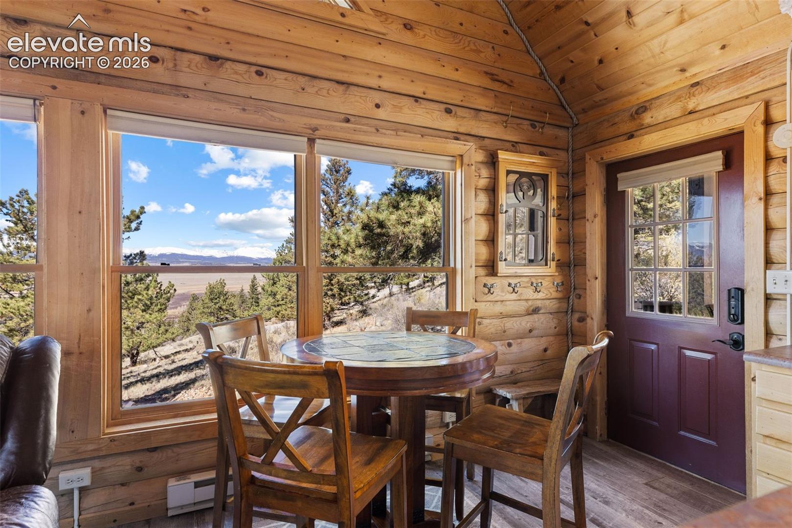 Interior featuring exposed log walls, a cathedral ceiling, wood-finish flooring, and expansive windows showcasing a mountainous landscape
