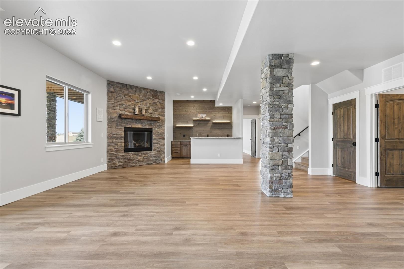 Spacious interior with wood-finish flooring, a stone-accented fireplace with a wood mantel, recessed lighting, and a stone-wrapped support column