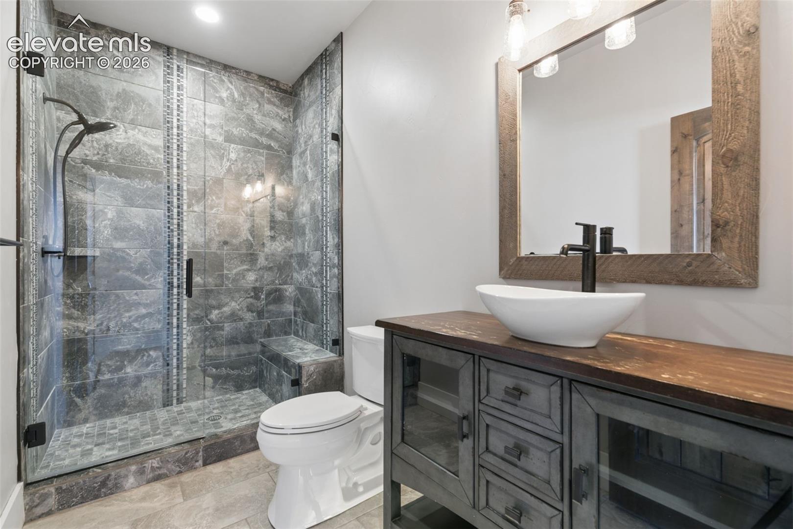 Glass-enclosed shower with stone-look tile, a built-in bench, and a rain showerhead