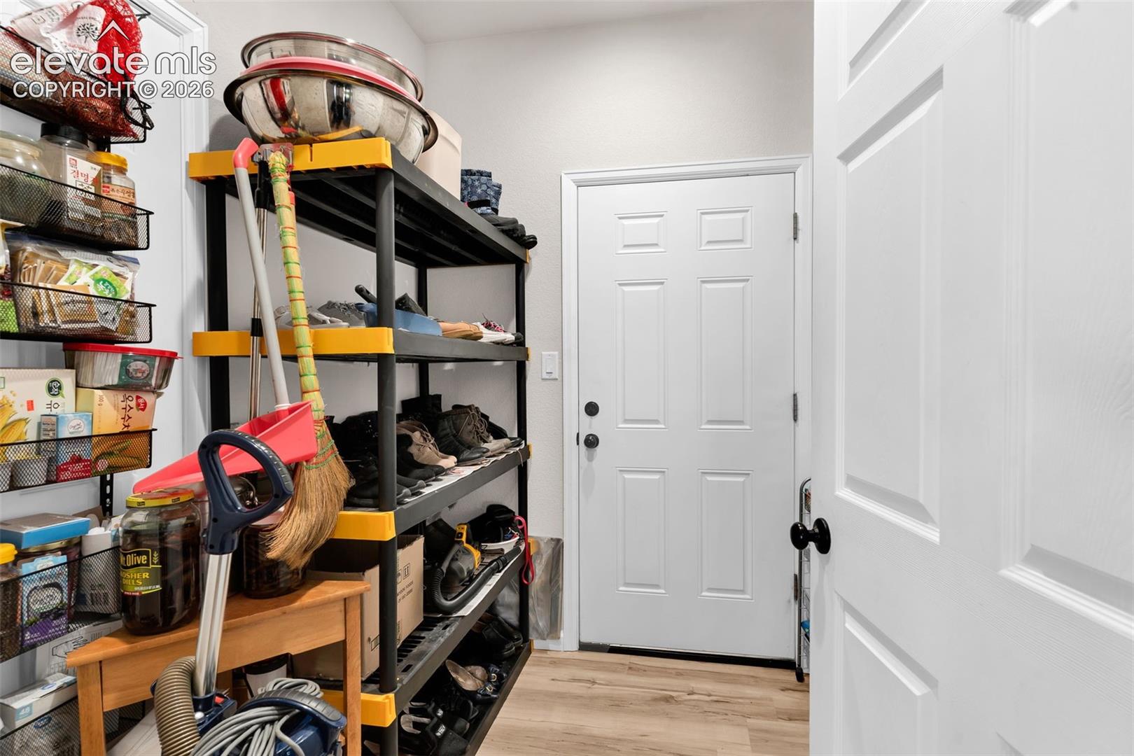 Utility room featuring light wood-finish flooring, white walls, and a paneled door with black hardware