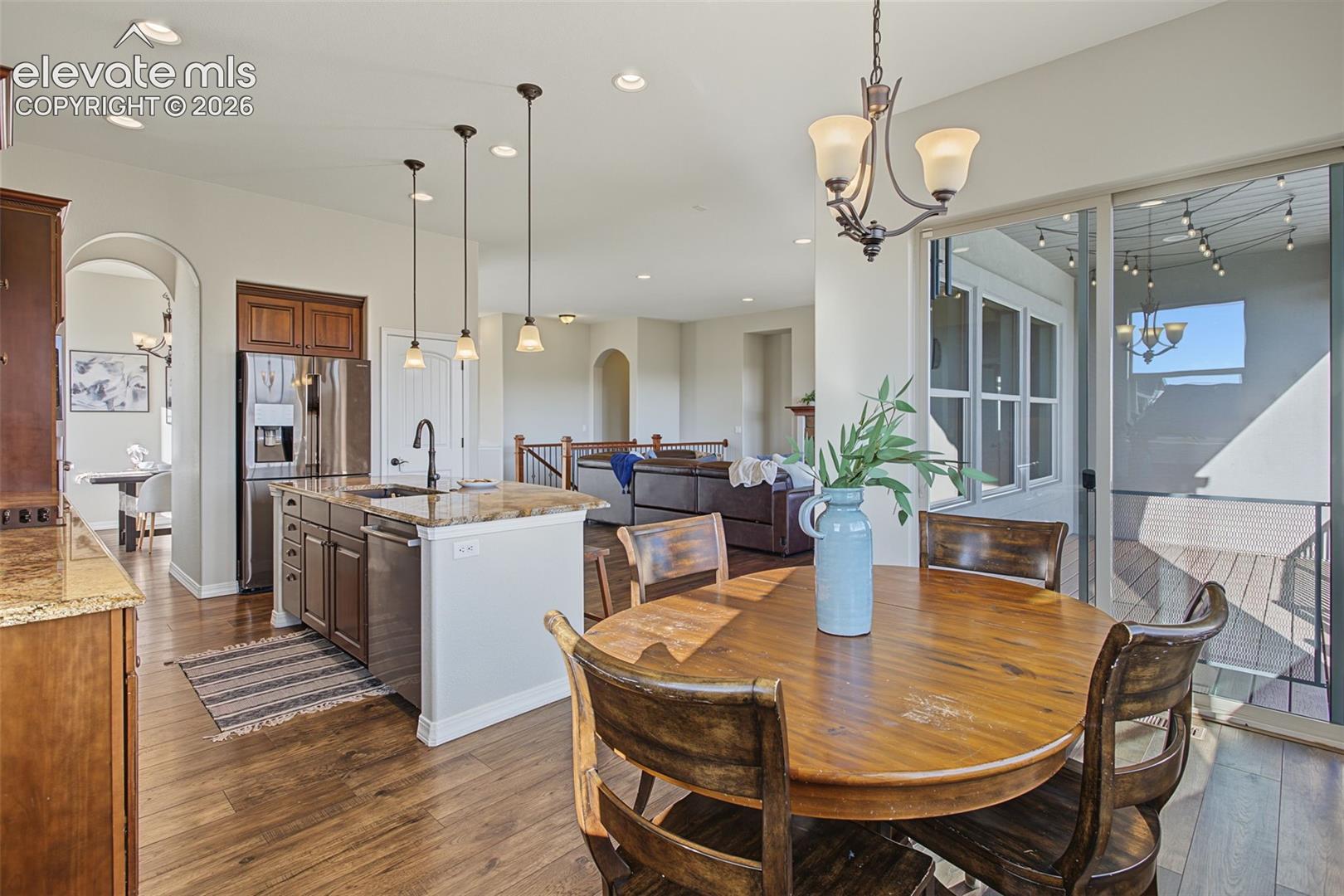 Kitchen featuring dark wood cabinetry, stone countertops, an island with pendant lighting, and wood-finish flooring