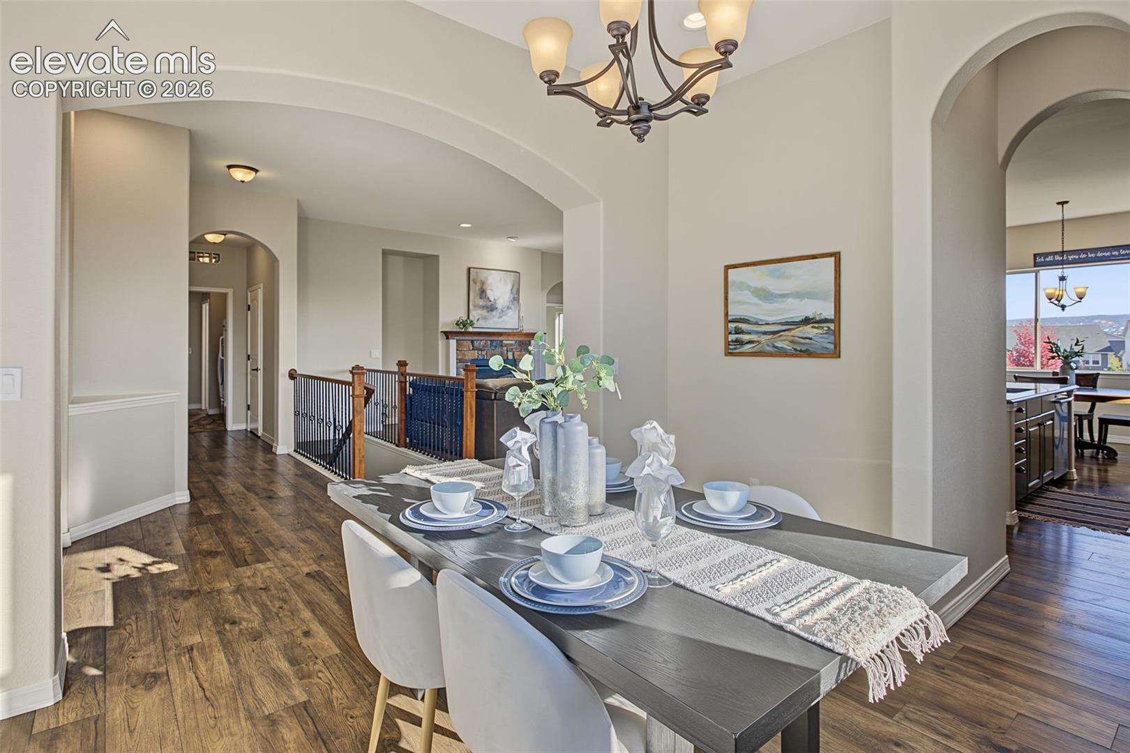 Open-concept interior featuring arched doorways, wood-finish flooring, iron spindle railing, and decorative multi-light chandelier
