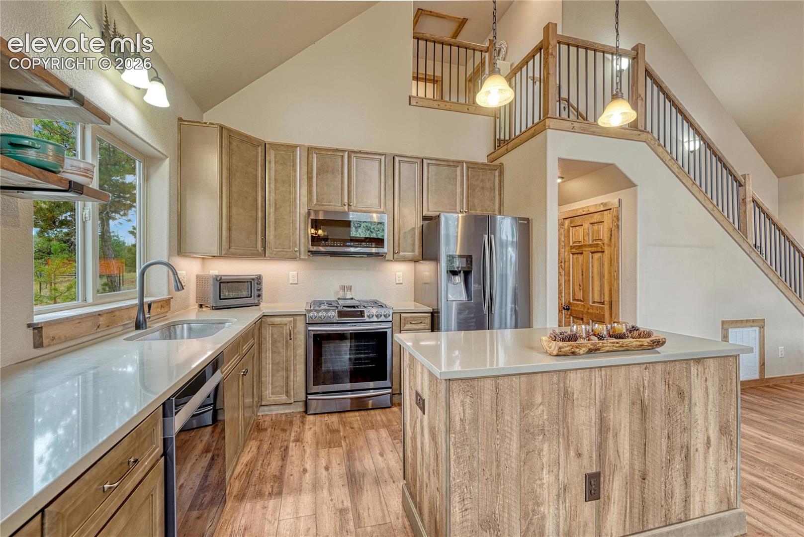 Kitchen featuring wood-finish cabinetry, quartz countertops, stainless steel appliances, a center island, and vaulted ceilings with a wooden railed loft