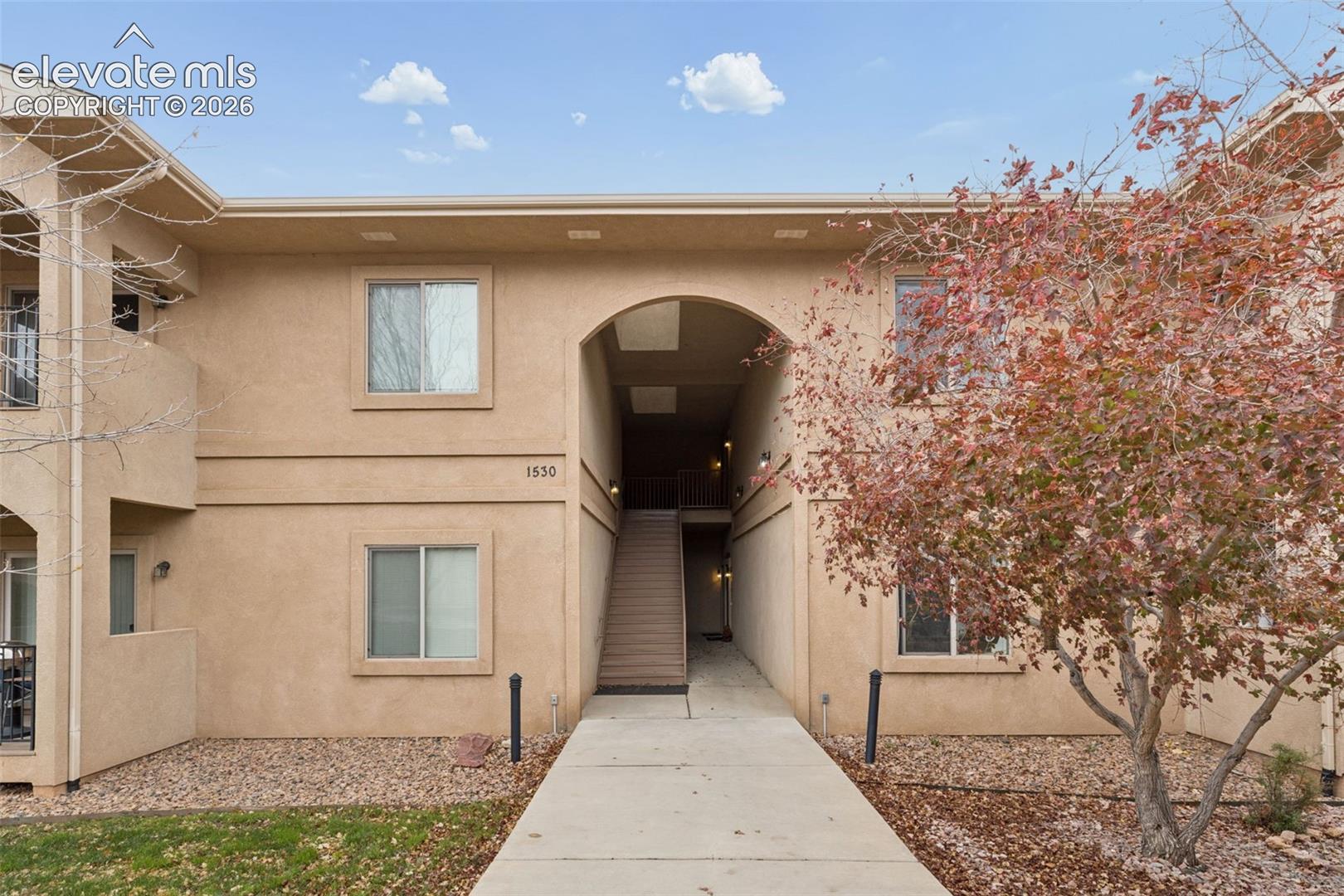 Stucco exterior featuring an arched entryway, double-story facade, and concrete pathway