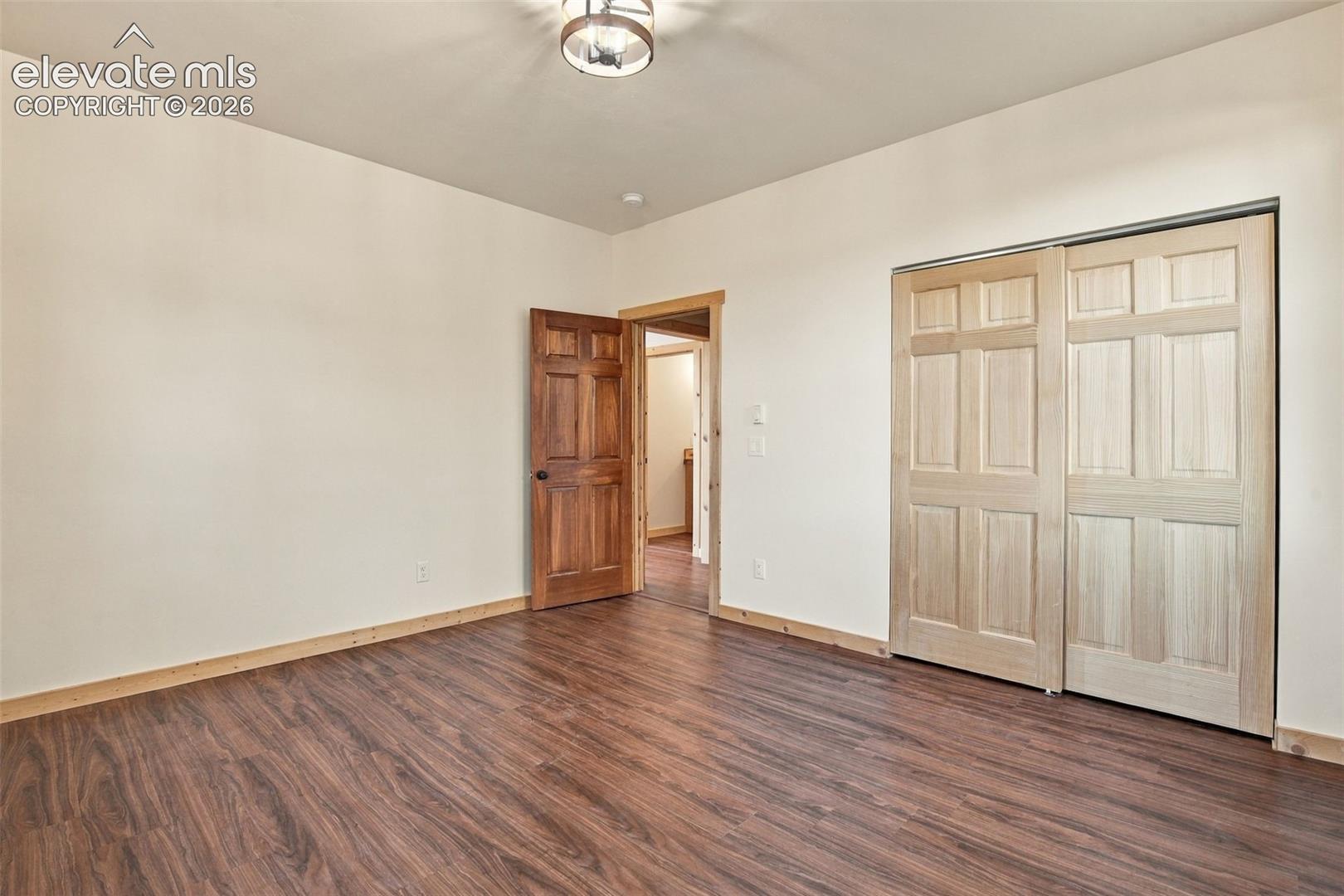 Wood-finish flooring, six-panel wood door, light-toned sliding closet doors, and a decorative semi-flush mount light fixture