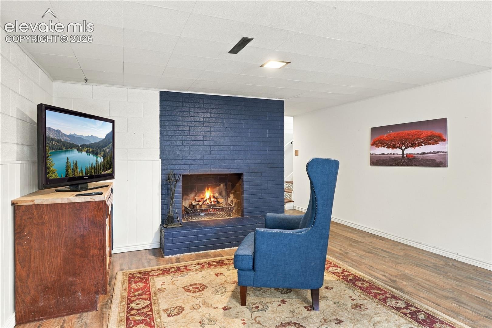 Painted brick fireplace, wood-finish flooring, and white-painted concrete masonry wall