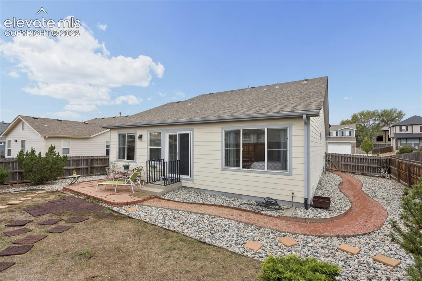 Exterior siding with multiple windows and a sliding glass door out to a flagstone patio.