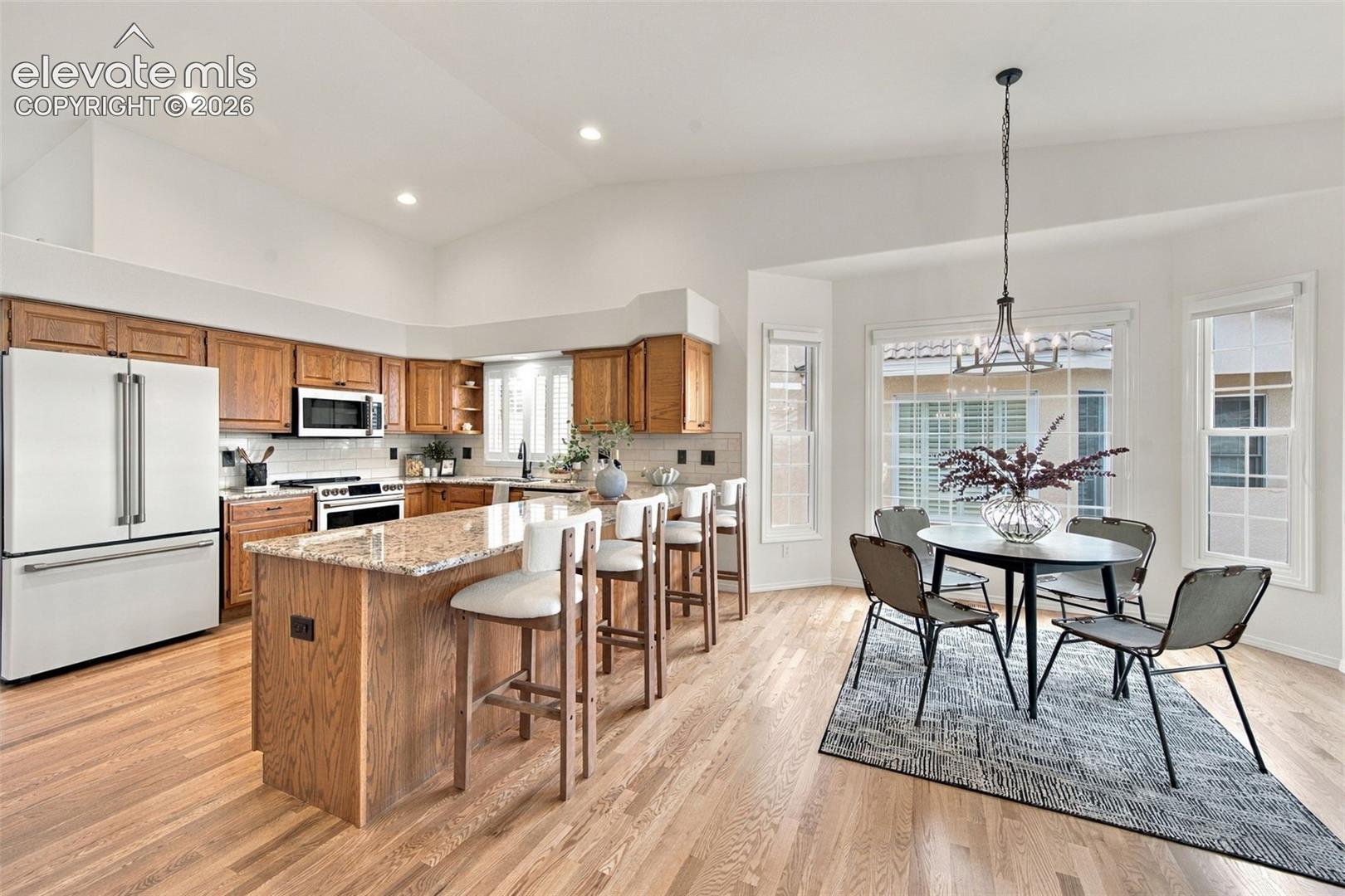 Kitchen featuring stained wood cabinetry, stone countertops, an oversized center island, vaulted ceilings, and wood-finish flooring